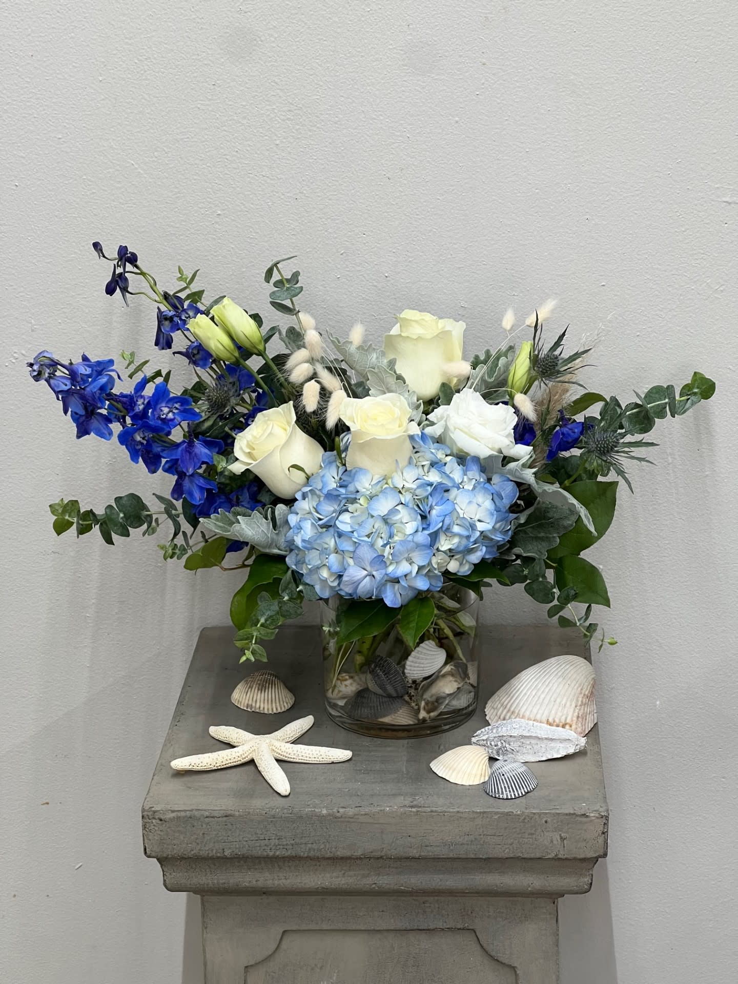 Blue and white floral arrangement in a glass vase with seashells and a starfish