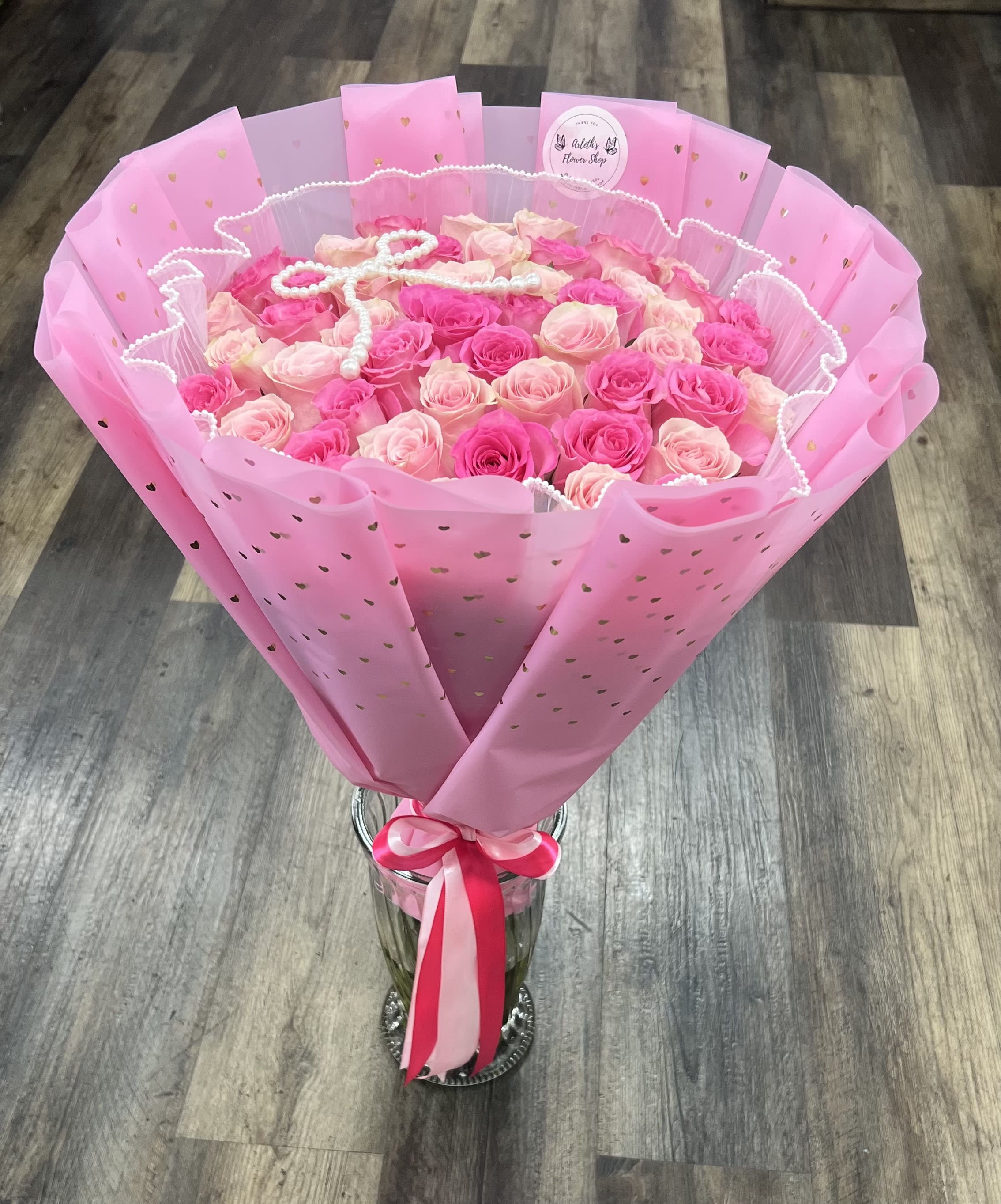 Pink and blush rose bouquet wrapped in pink paper with a ribbon, in a glass vase