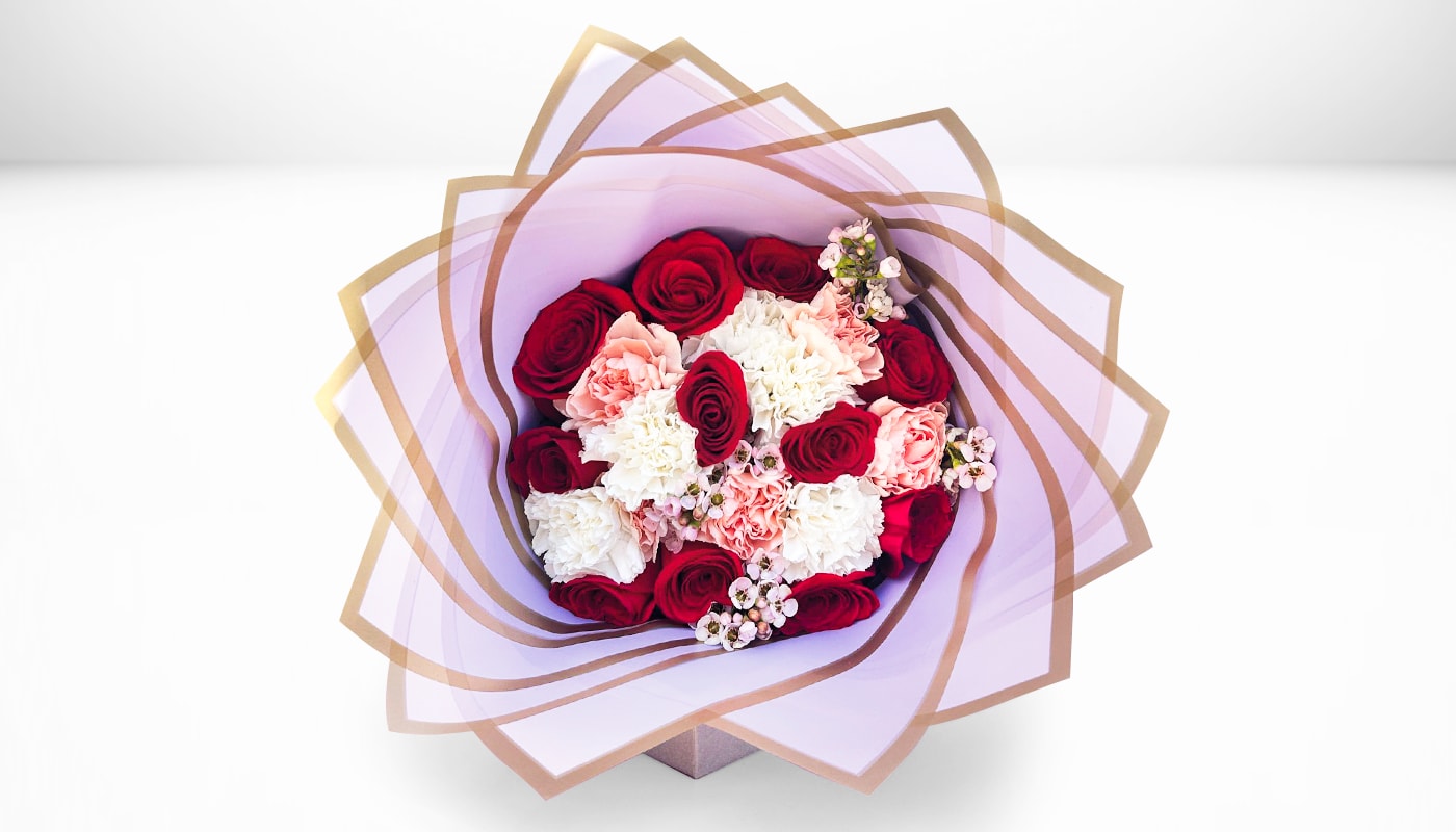 Bouquet of red roses, pink carnations, and white blooms wrapped in lavender paper