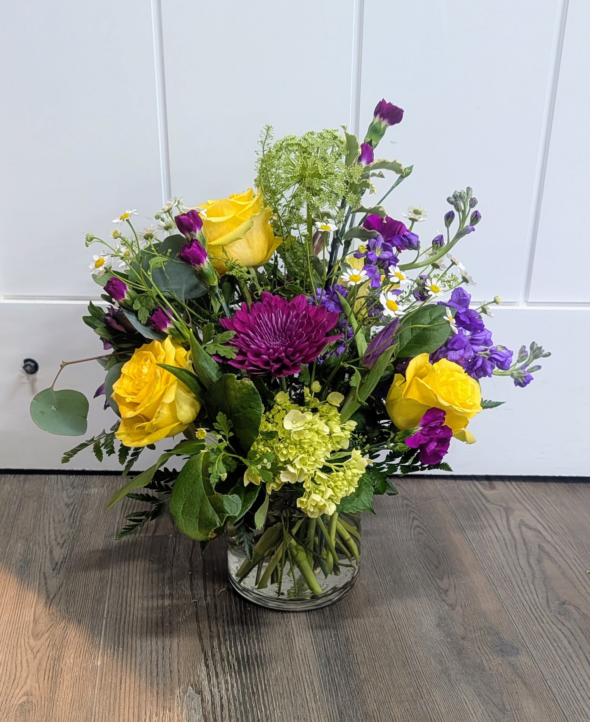 Sweet Surprise - Cylinder vase includes yellow roses, purple mums, stock green hydrangea, alstroemeria, mini carnations, filler &amp; greens