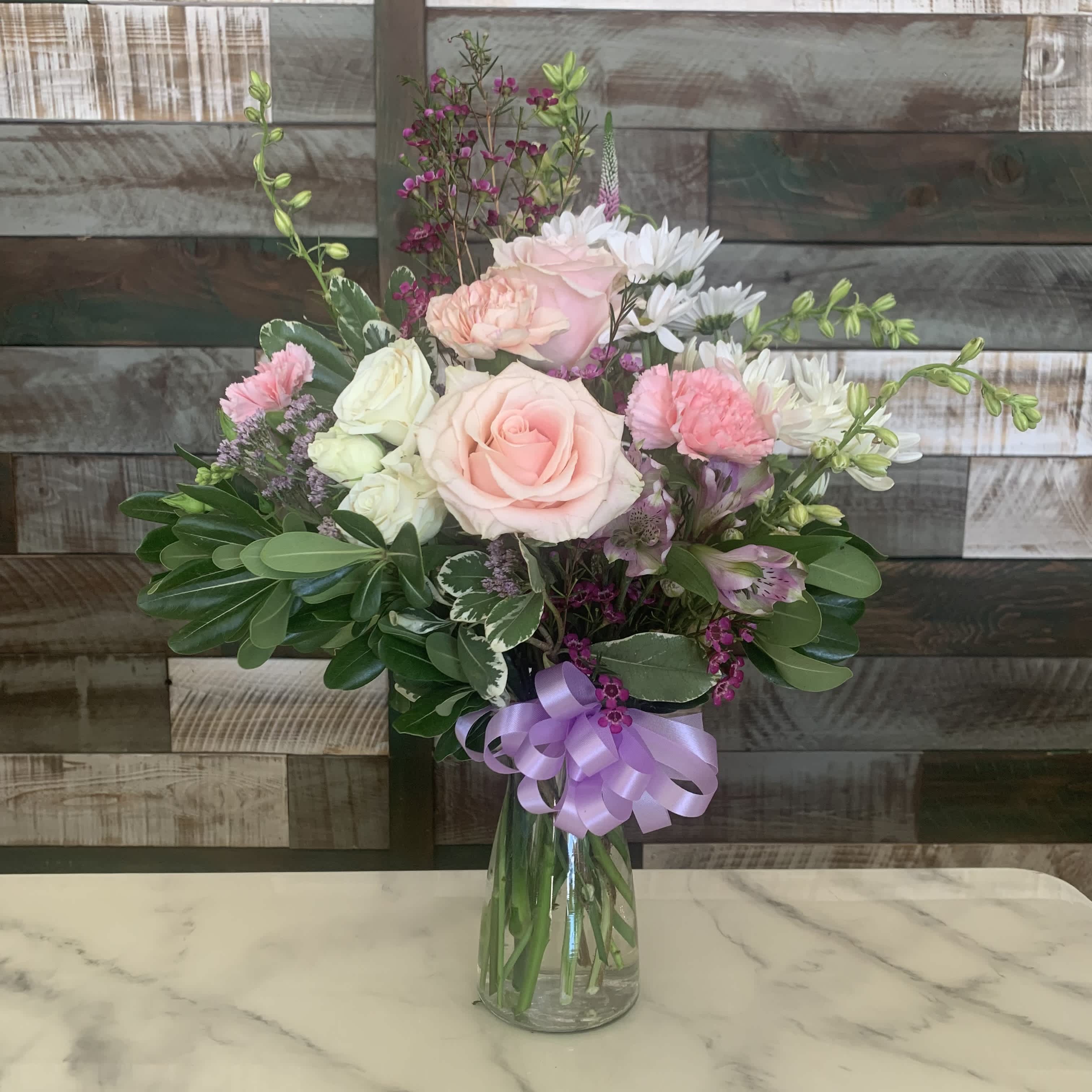 Pink and white flower bouquet in a glass vase with a lavender ribbon