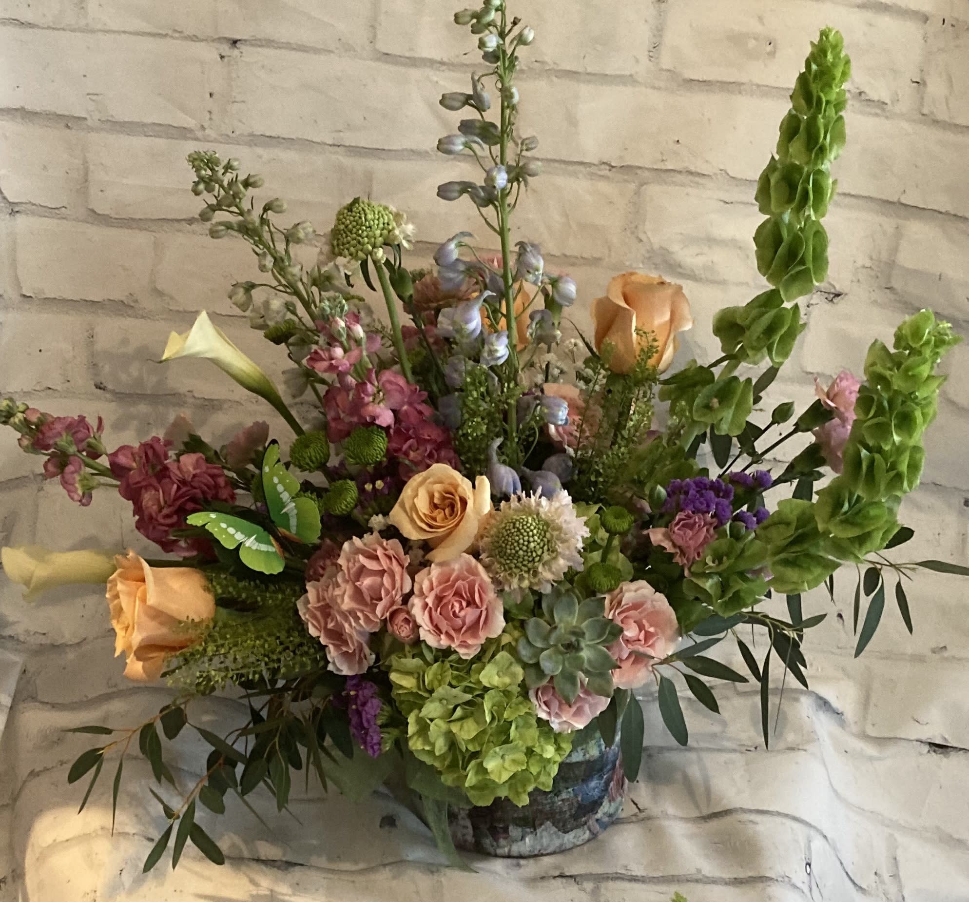 Mixed bouquet with peach roses, pink blooms, and tall green spikes in a vase