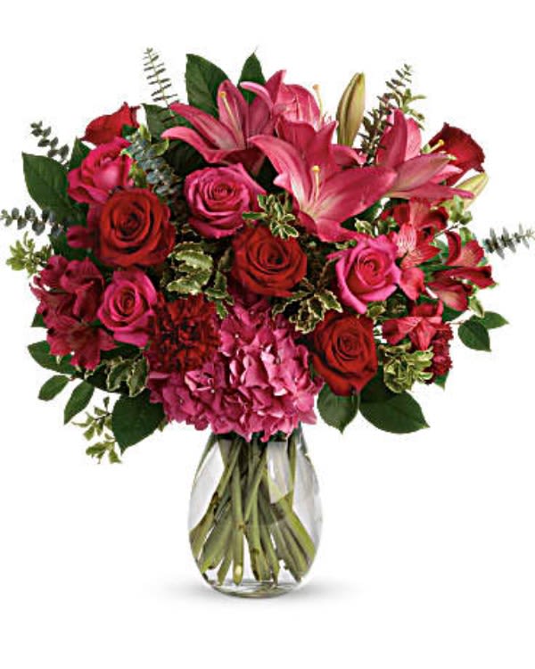 The Nastassia Luna  - A luxurious bouquet that’s sure to leave your special someone absolutely love struck! There’s no denying the dramatic beauty of these radiant, red hot roses, hydrangea and lilies. This luxe arrangement includes pink hydrangea, hot pink roses, red roses, dark pink asiatic lilies, dark pink alstroemeria, maroon carnations, and fresh greens. Delivered in a clear glass vase.