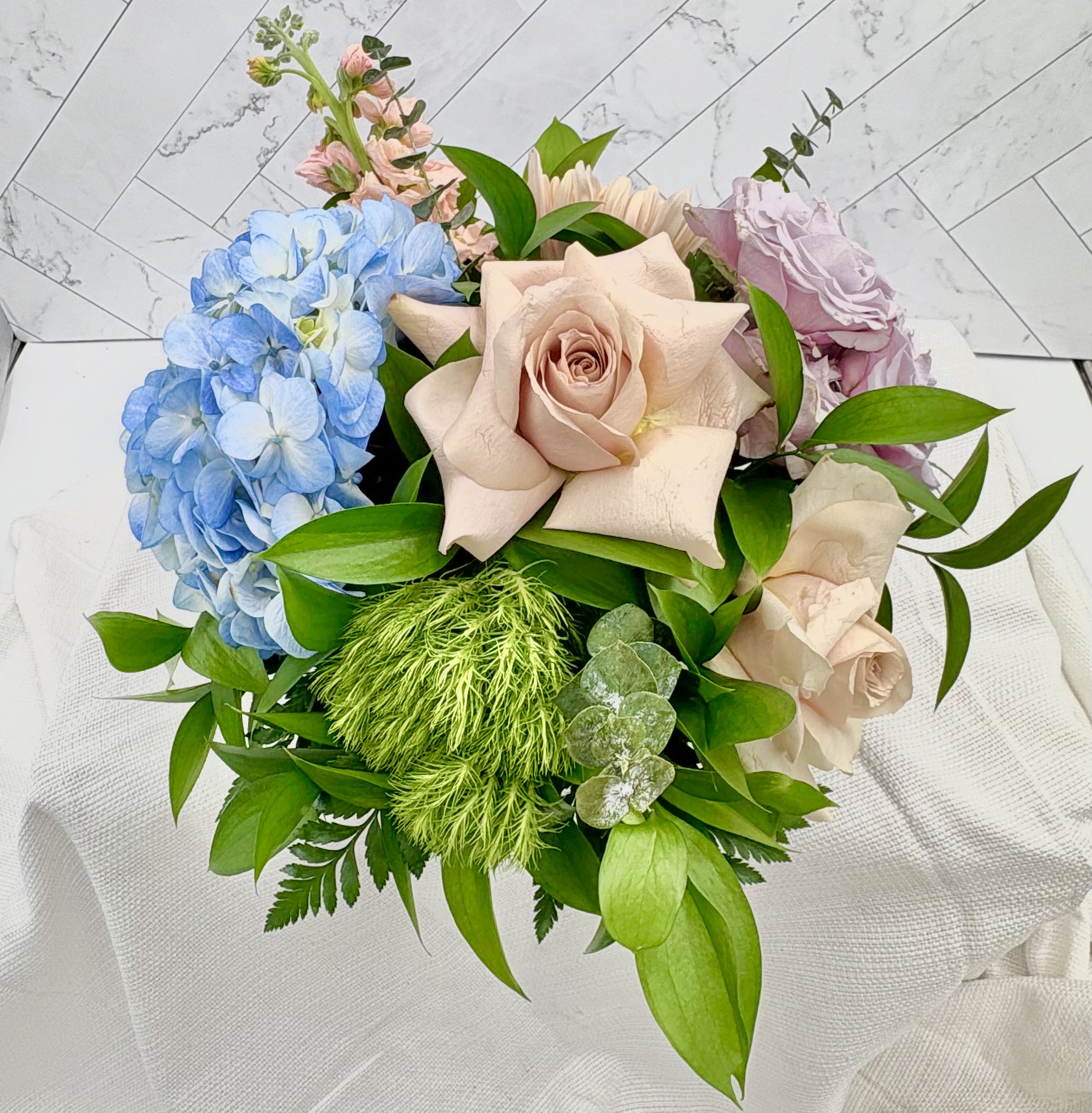 The Jersey Shore - Quicksand roses, blue hydrangeas &amp; green dianthus in a summery low arrangement-vibrant coastal tones. See our thoughtful gift section to add on any gift item to be delivered with your arrangement.