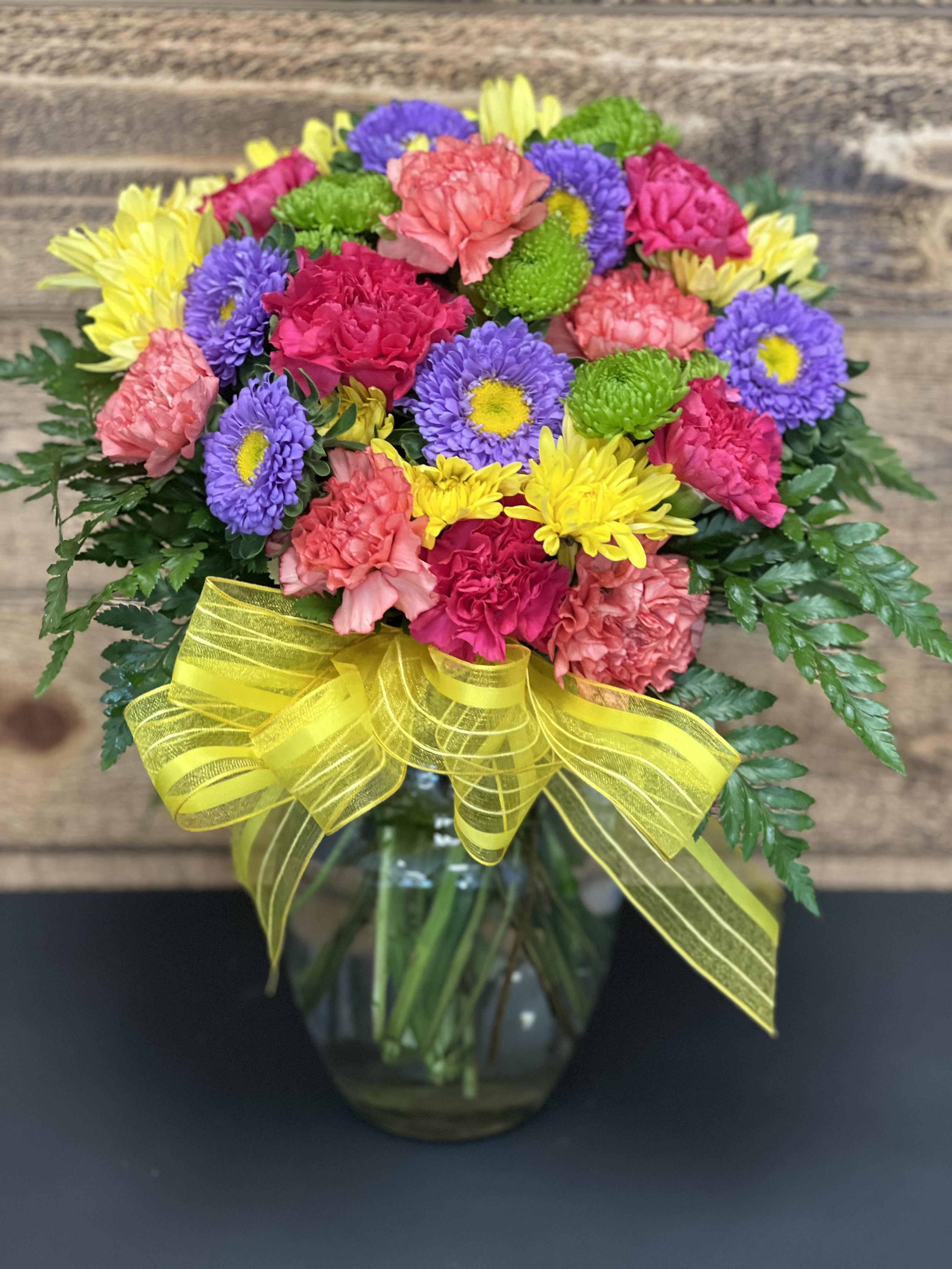Colorful mixed bouquet in a glass vase with a yellow ribbon