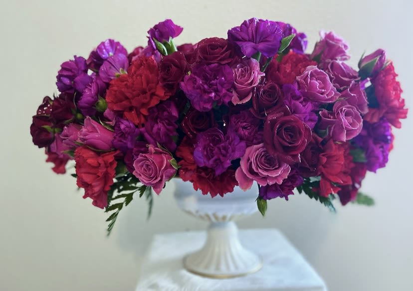 Purple and pink floral arrangement in a white pedestal vase