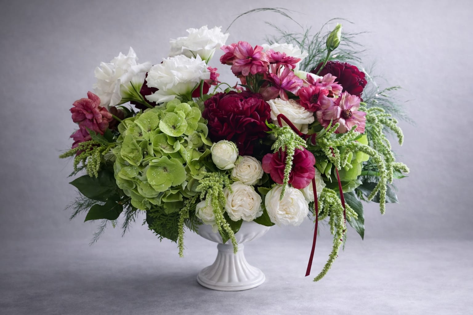 Mixed bouquet in a white pedestal vase with green hydrangea, white roses, and pink blooms