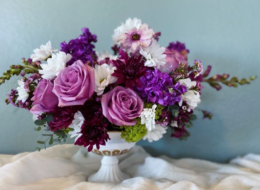 Purple and white floral arrangement in a white pedestal vase