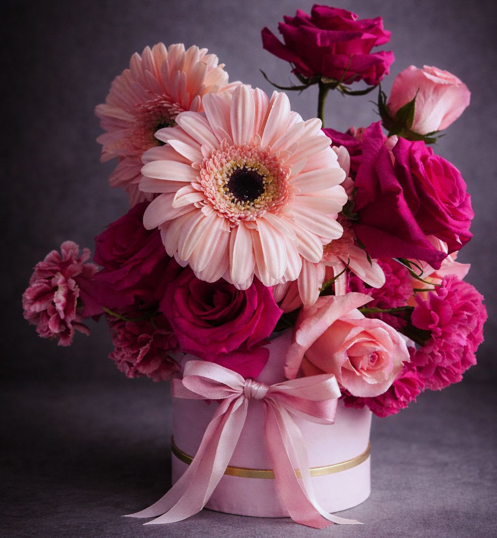 Pink and magenta flower arrangement in a round box with a ribbon