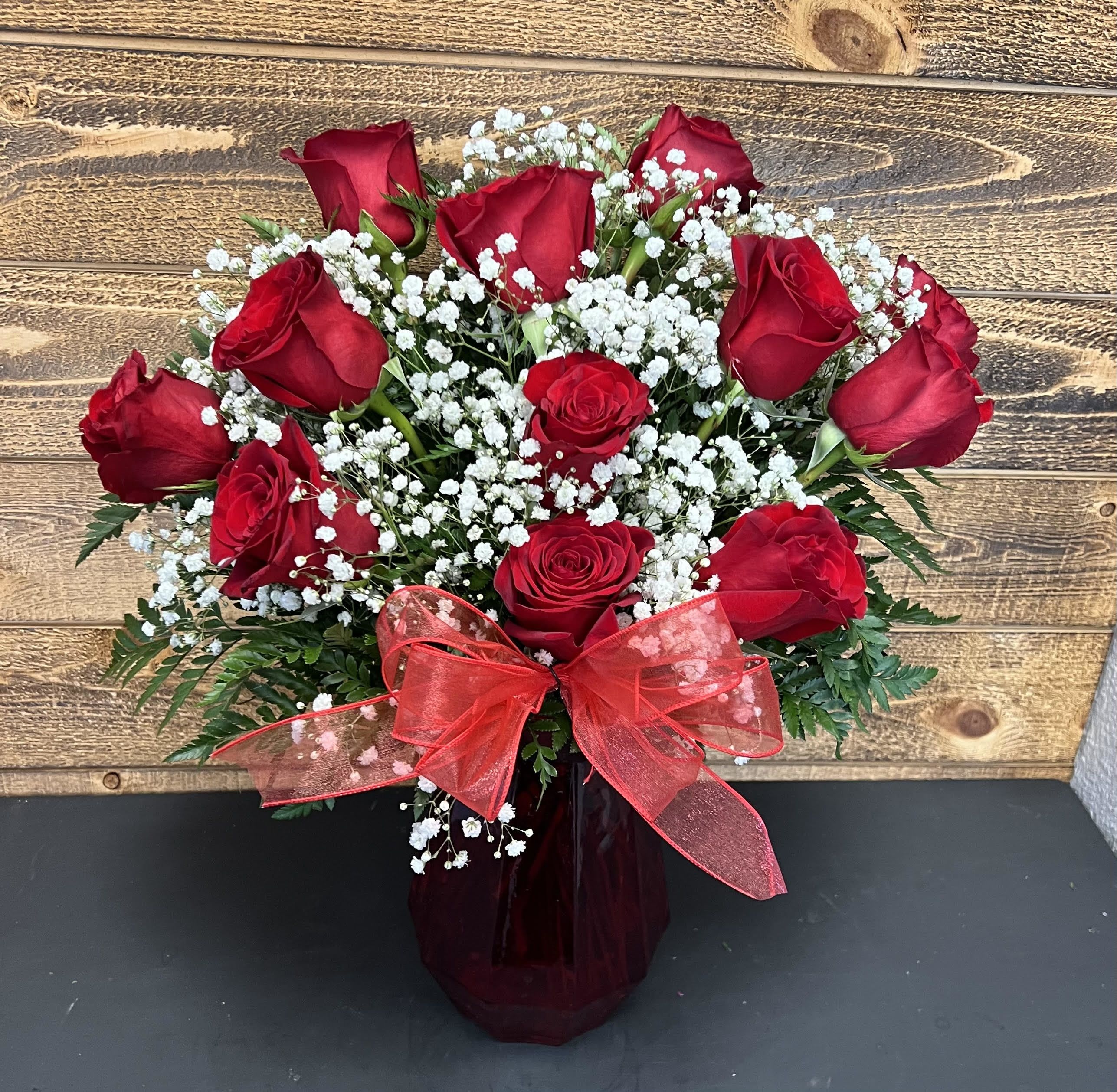 Red roses with white baby's breath in a dark vase and red bow