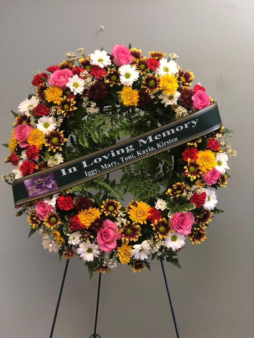 Circular sympathy wreath with pink roses, daisies, and mums on a stand