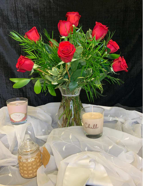Red roses in a clear glass vase with candles on white fabric