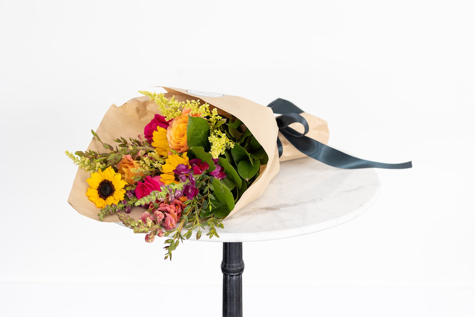 Bouquet of sunflowers, roses, and mixed blooms wrapped in tan paper