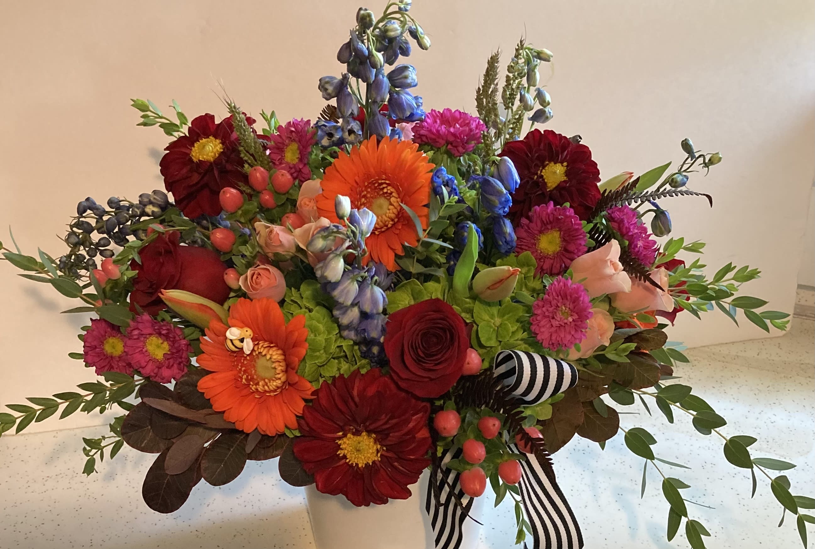 Mixed bouquet of bright flowers in a white vase with striped ribbon