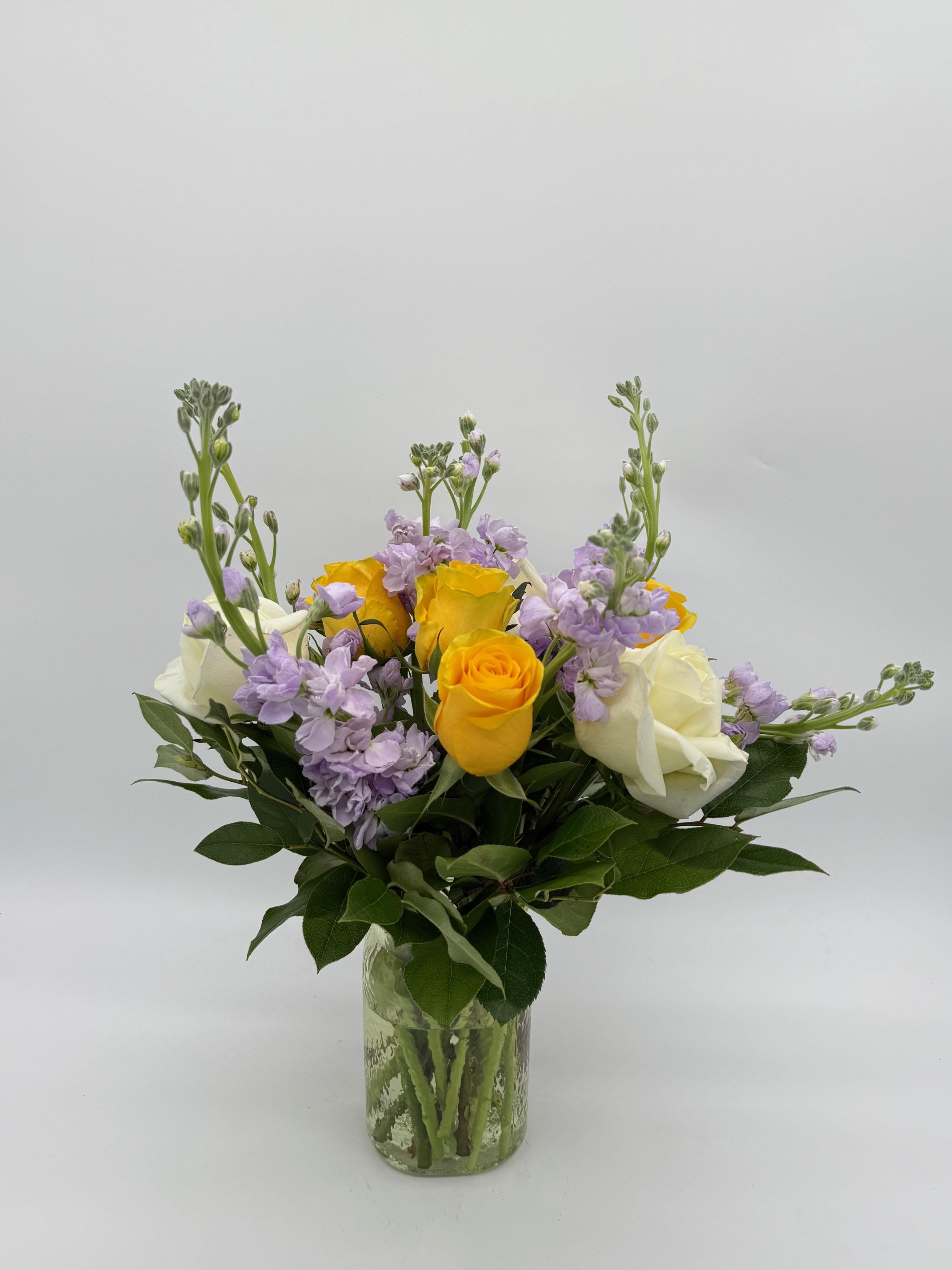 Bouquet of yellow and white roses with lavender flowers in a glass vase