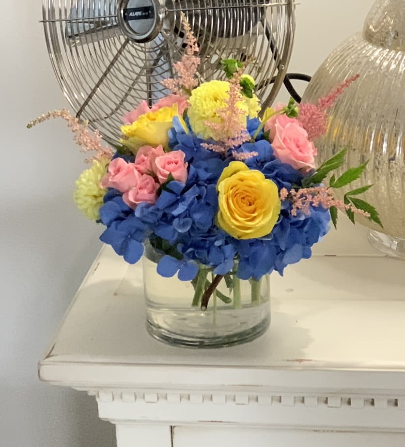 Bouquet of blue hydrangeas, pink roses, and yellow roses in a glass vase