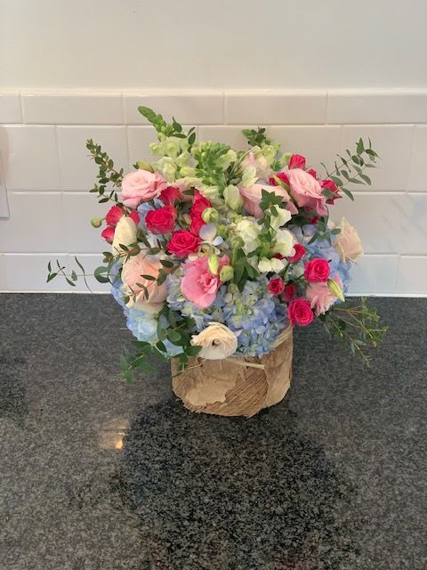 Mixed bouquet of pink roses, blue hydrangeas, and white blooms in a wrapped container