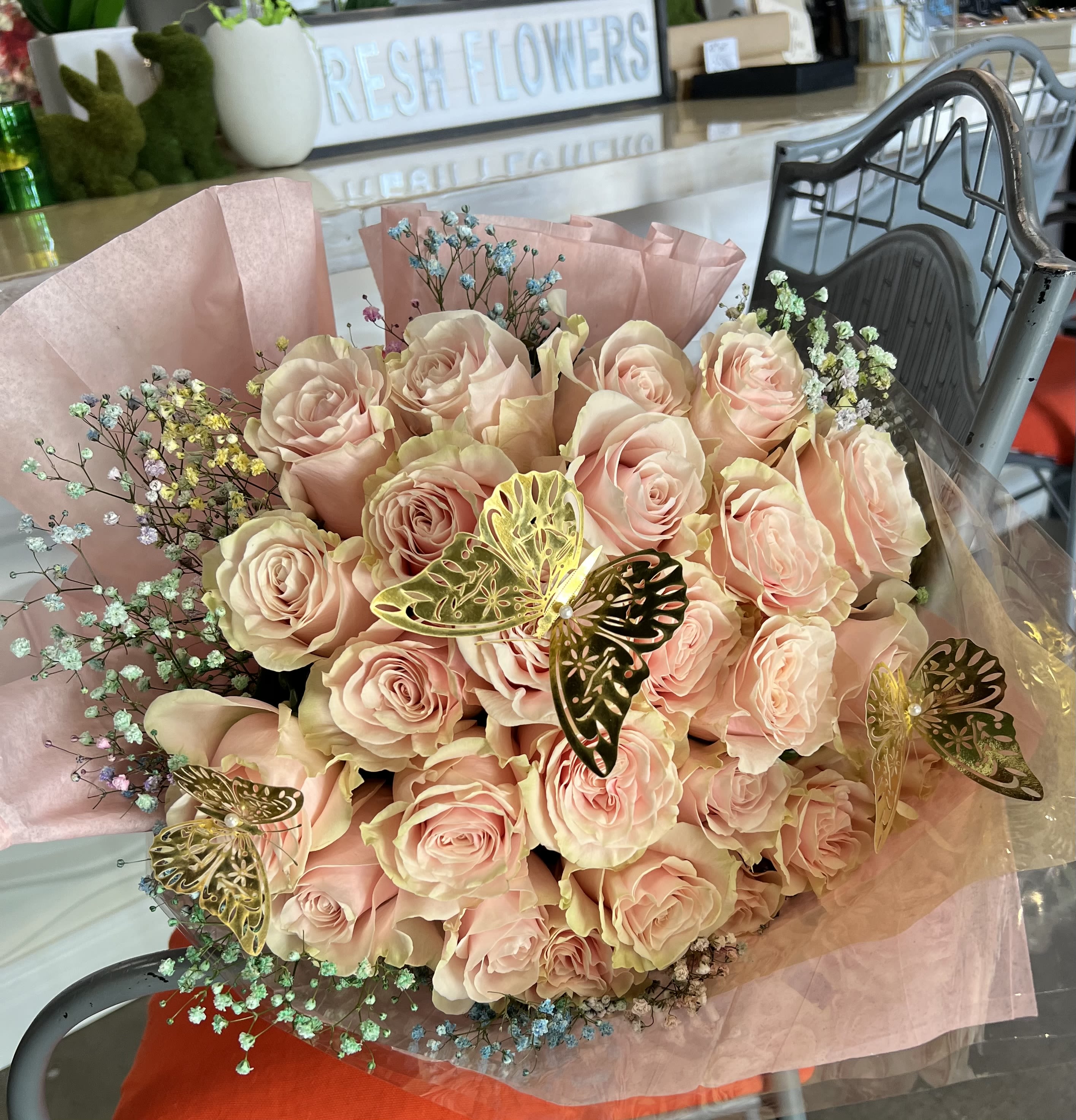 Pink Buchoen Bouquet - A cloud of pale blush-pink roses makes an immediate, romantic impression in this hand-tied flower arrangement-perfect as a birthday bouquet, anniversary roses, or a Mother's Day gift to show deep affection. Soft pastel filler blooms and metallic butterfly picks add an airy, whimsical edge so the recipient will feel genuinely celebrated and seen, whether you're marking love and romance or sending a thoughtful "just because" surprise.  The bouquet is built from many tightly clustered pale pink roses with small sprays of pastel baby's breath (and other delicate fillers) around the perimeter for light texture. It arrives wrapped in layered pink tissue and pink paper with clear plastic wrap to protect the stems, and finished with decorative butterfly picks for a feminine, gift-ready presentation. Sized as a full, rounded hand-tied bouquet, it's an elegant choice for Valentine's Day, thinking-of-you moments, or simply to make someone feel cherished; keep stems trimmed and fresh water changed daily to extend bloom life.