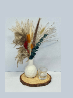 Dried floral arrangement in a white vase on a wood slice with a small glass candle holder