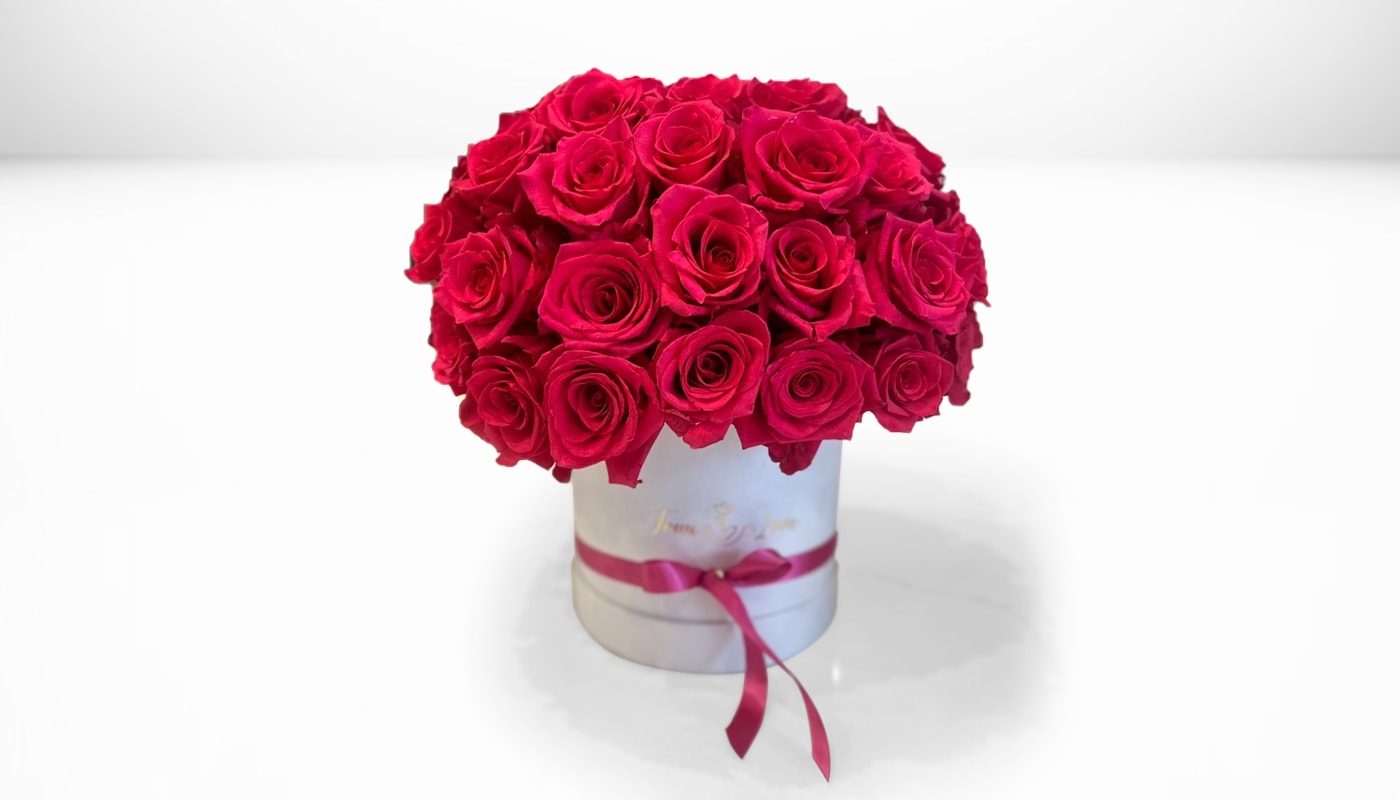 Round bouquet of red roses in a white hat box with a pink ribbon