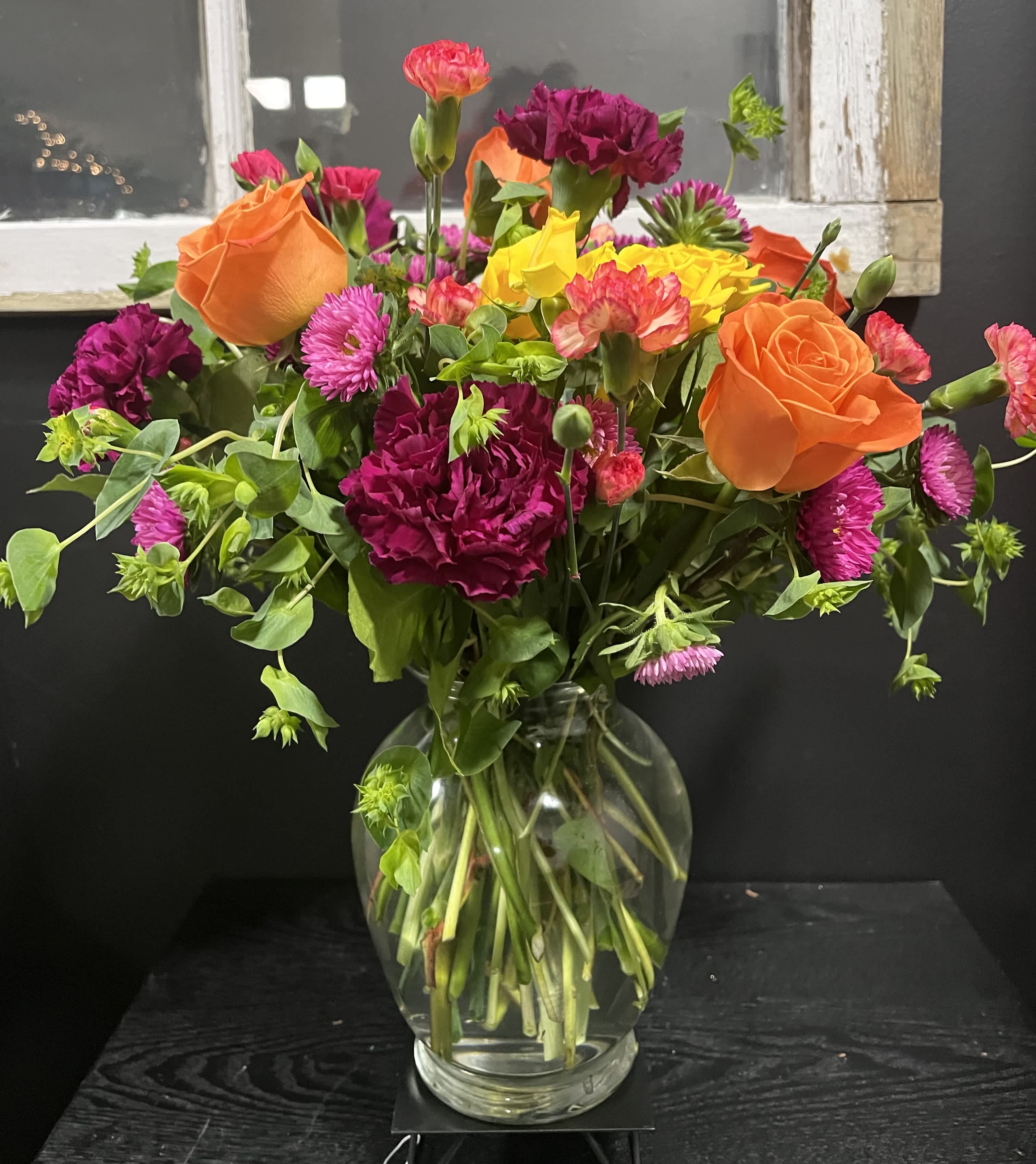 Mixed bouquet of orange roses, magenta carnations, and yellow blooms in a glass vase