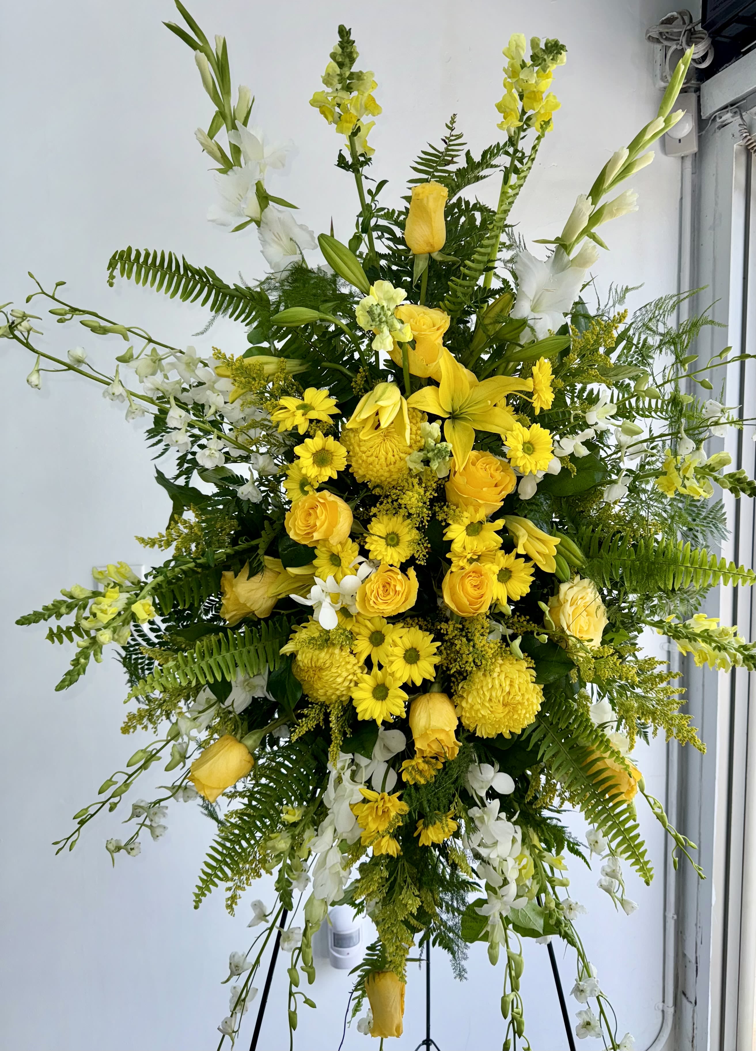 Tall yellow and white floral standing spray on a black easel
