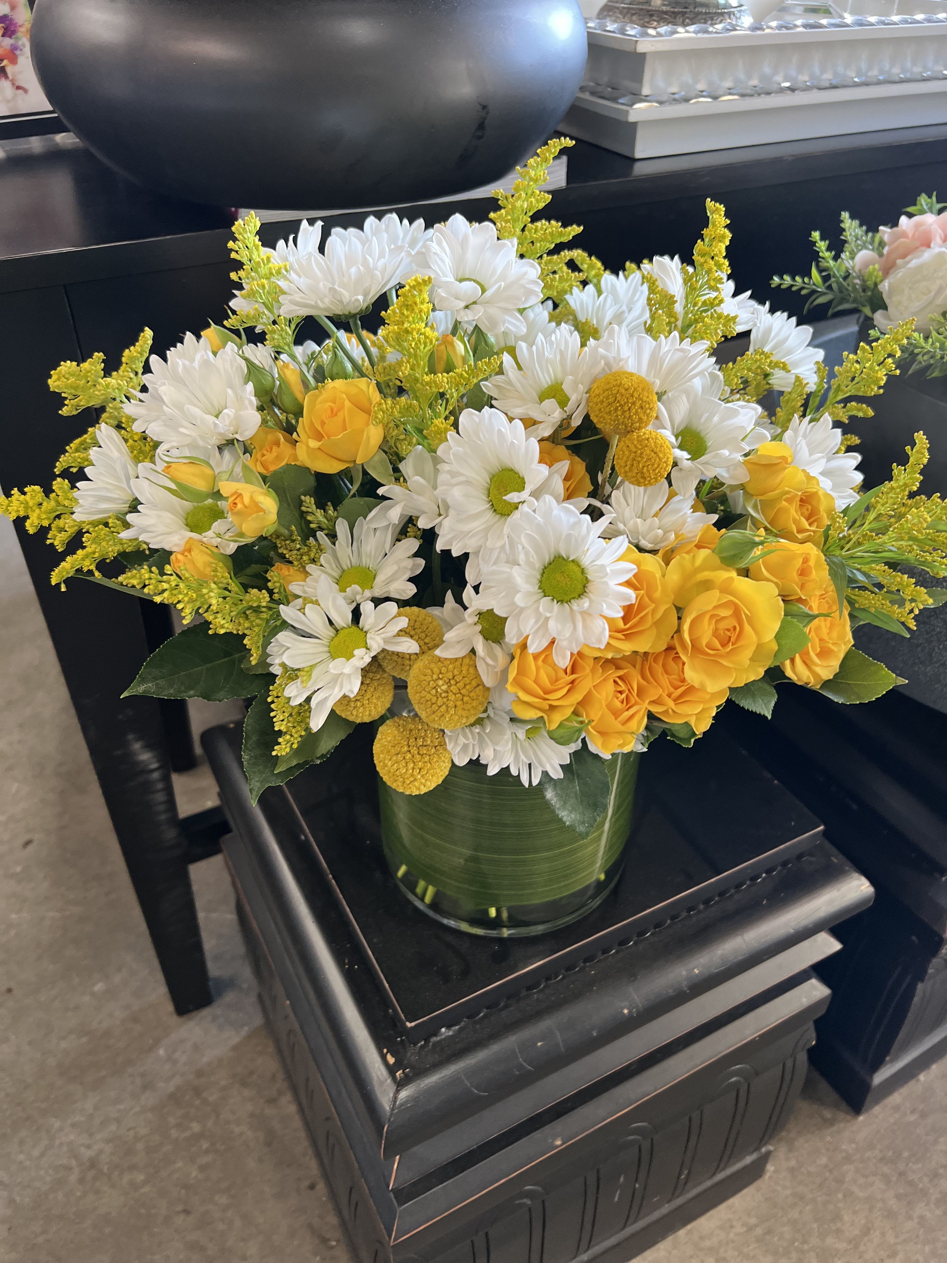 Sunshine  - Bright yellow roses take center stage in this Sunshine flower arrangement, a cheerful bouquet perfect for a birthday bouquet, spring celebration, or a bright thank-you gesture. The sunny mix of yellow, white, and fresh green reads as optimism in bloom-ideal for the person you want to make smile or to bring light into a room.  Clusters of white daisy-like chrysanthemums and small yellow button mums surround the roses, creating a full, rounded design with lively contrast between crisp white petals and warm golden tones. The stems are gathered in a clear cylindrical glass vase for a clean, modern presentation that still feels natural and abundant; the arrangement sits low and elegant, easy to display on a kitchen table or office desk.  Send this to celebrate everyday moments, lift someone's spirits, or mark a springtime occasion-the recipient will feel genuinely seen by its bright, joyous presence. Care is simple: keep the glass vase filled with fresh water and trim stems every few days to extend vase life and maintain that just-picked freshness.