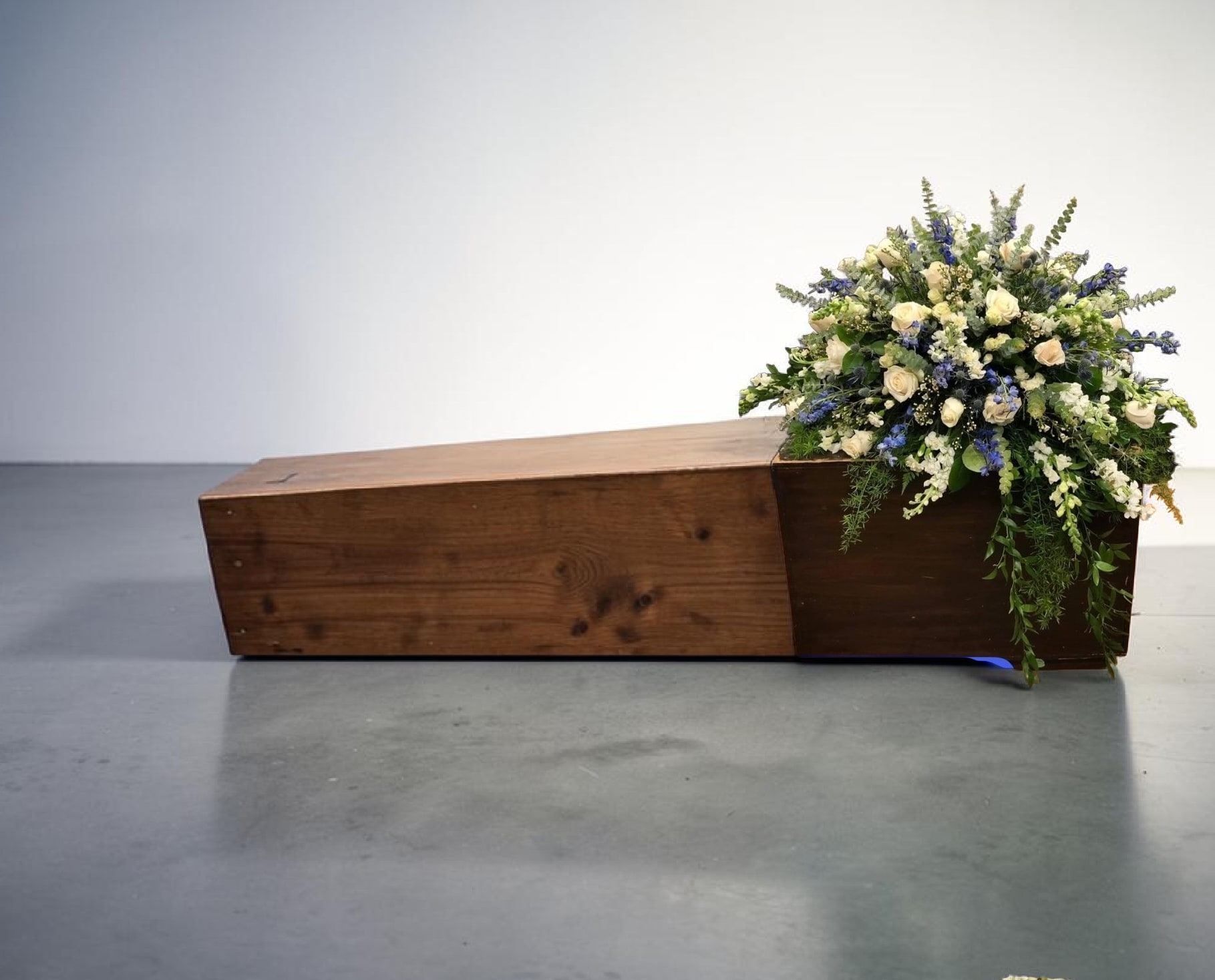 Serenity Garden Tribute - graceful sympathy arrangement featuring soft white roses and delicate blue blooms, elegantly arranged in a rustic wooden base. Designed to bring peace and comfort, this piece offers a serene expression of love, remembrance, and heartfelt condolences.
