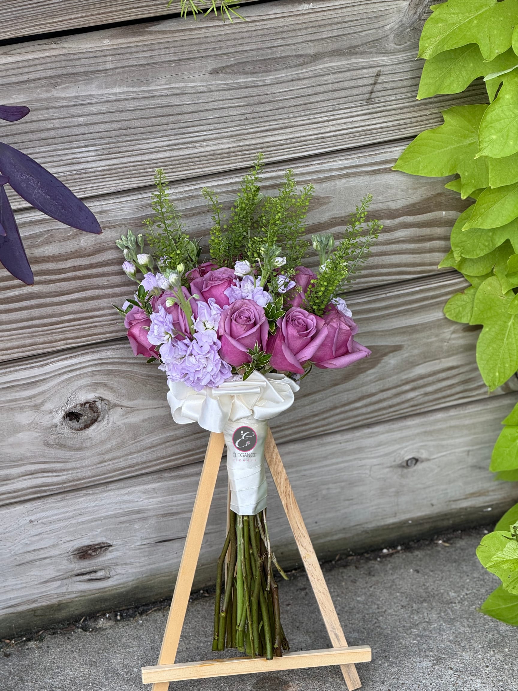 Pink rose bouquet with lavender flowers and white ribbon on a wooden stand