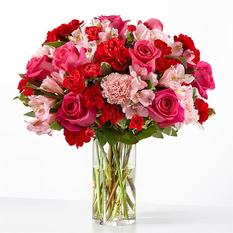 Bouquet of pink roses, red carnations, and pale alstroemeria in a clear glass vase