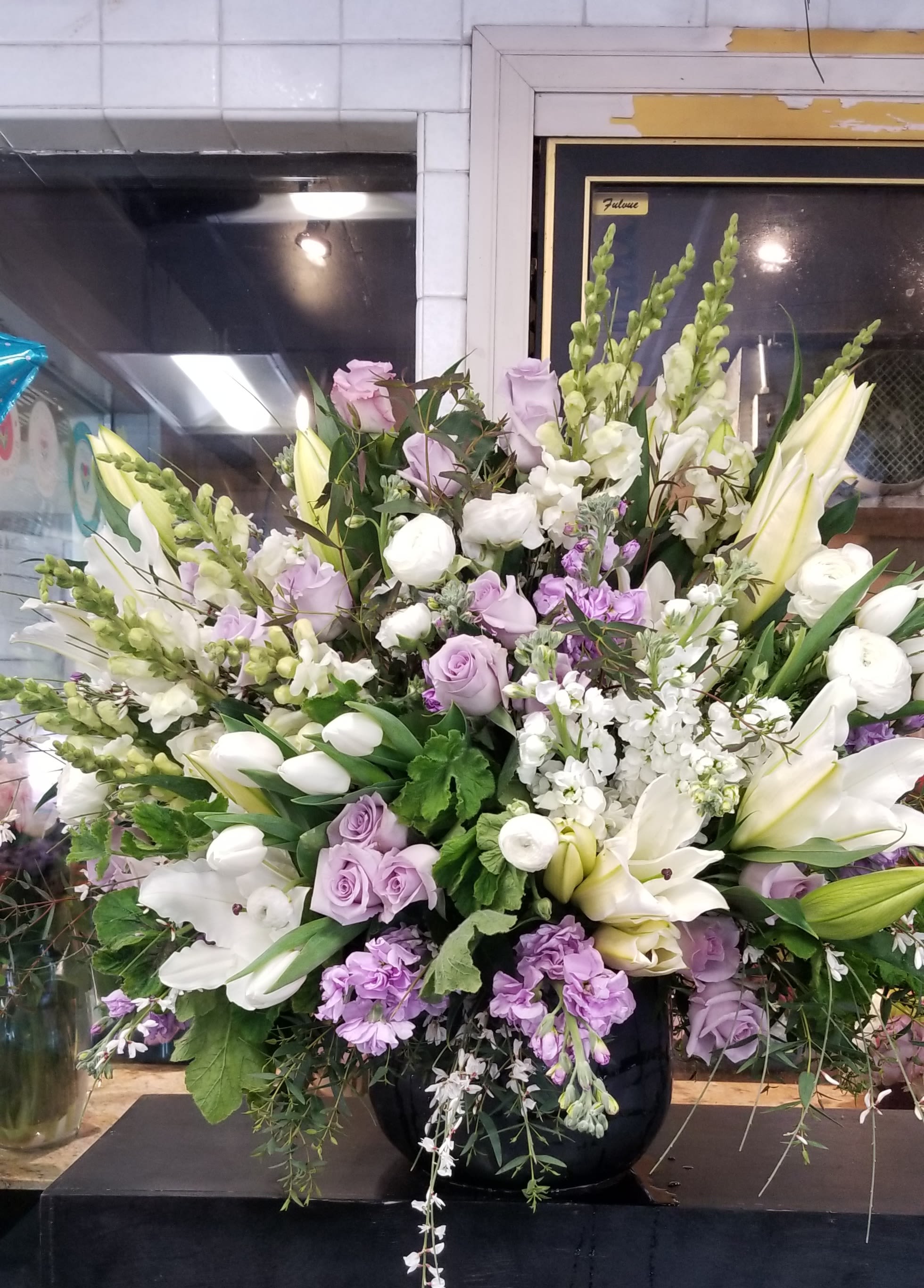 Large lavender and white floral arrangement in a black vase