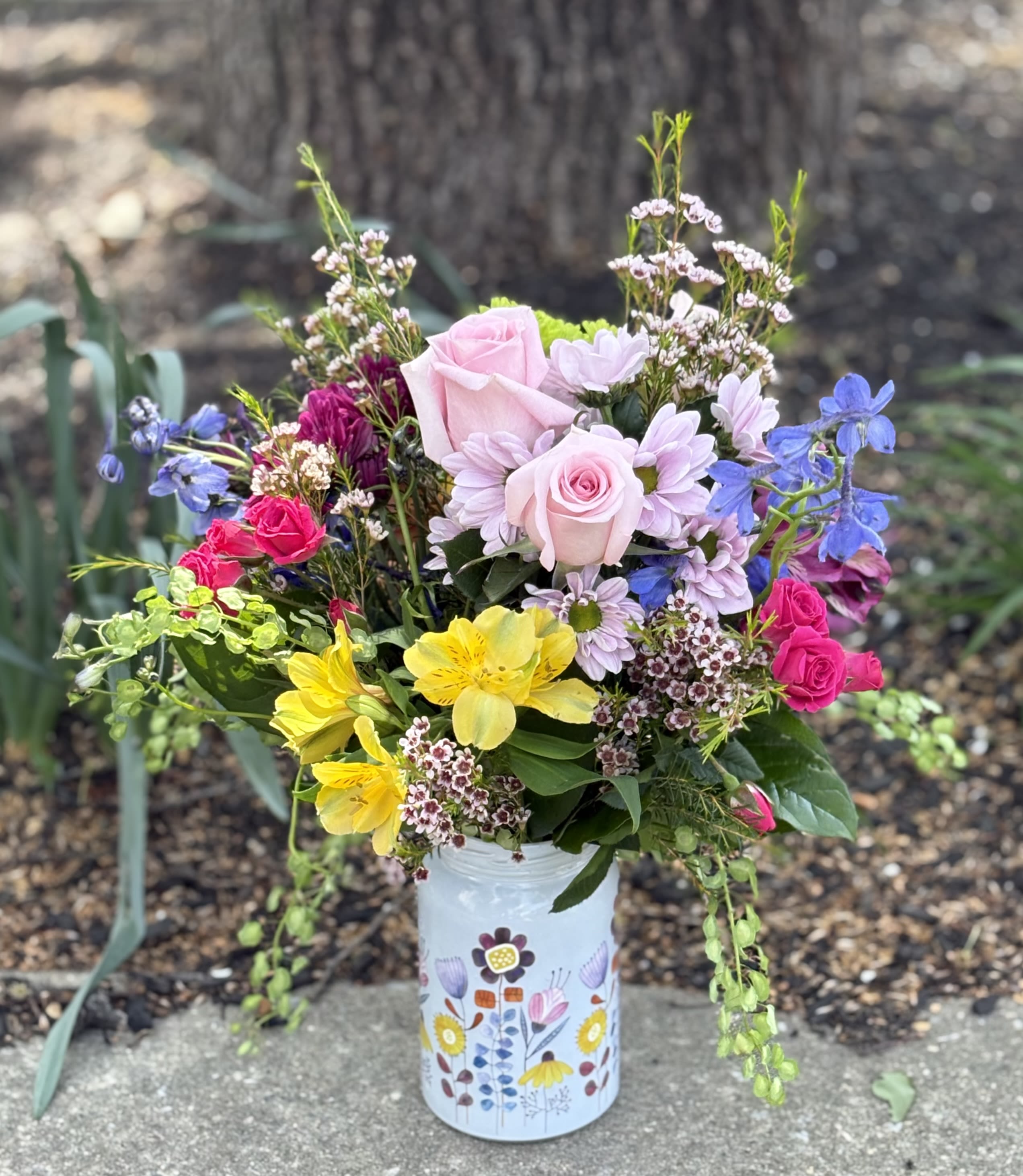 Wildflower Jar - A cheerful, garden-style arrangement bursting with fresh spring color. Roses take center stage, surrounded by delicate snapdragons, daisies, alstromeria and delphinium. This airy design is arranged in a whimsical floral-print vase, for a playful, feel-good finish - perfect for brightening any day!