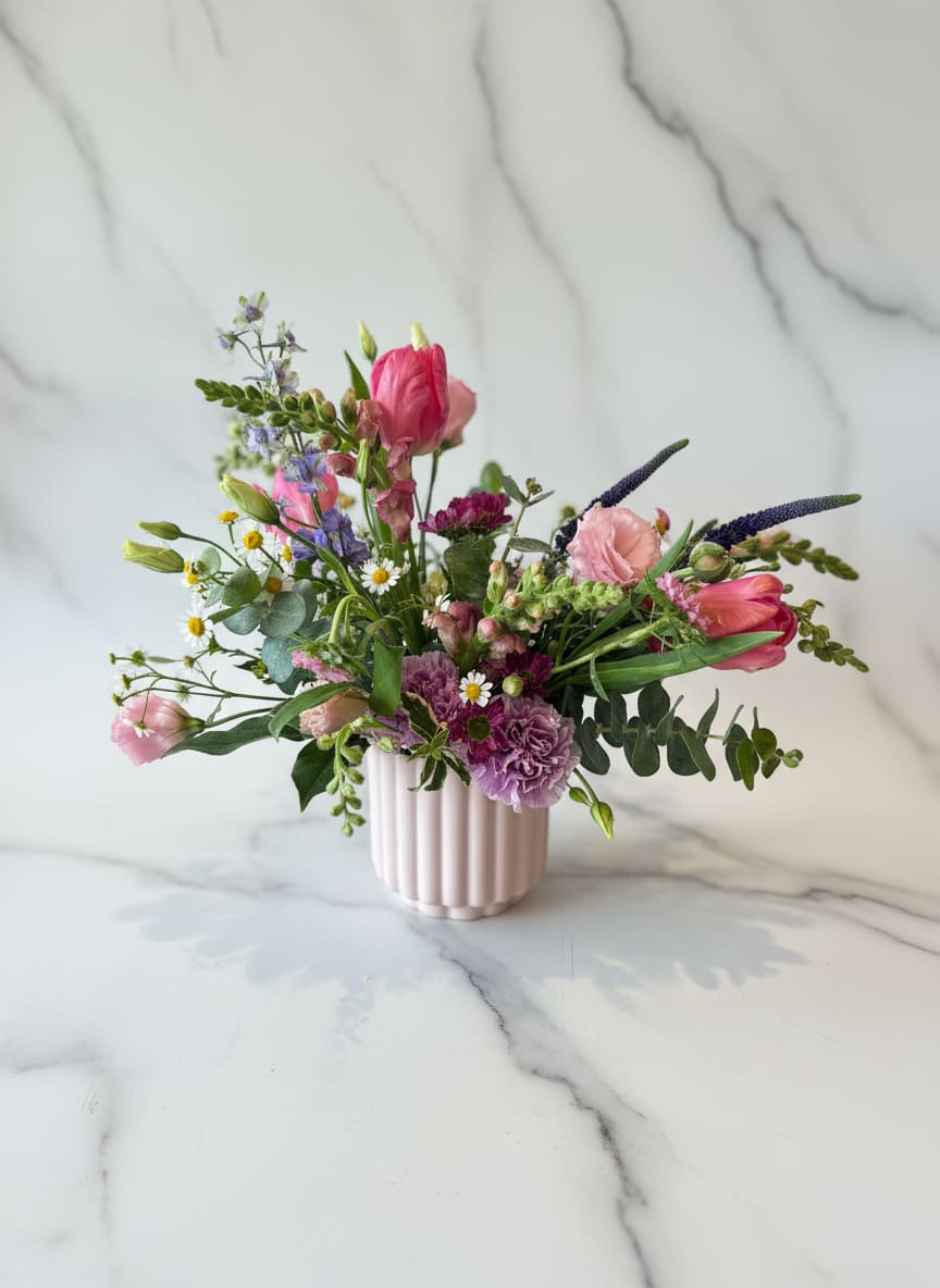Wildflower  - She belongs among wildflowers - for the free spirited soul, this arrangement is full of wild blooms such as chamomile, snapdragons, veronica and some other whimsical favorites. This is one of our newest favorites for those who prefer something just a bit unusual.  Design in a petal-pink ceramic container.   approx. 12x12