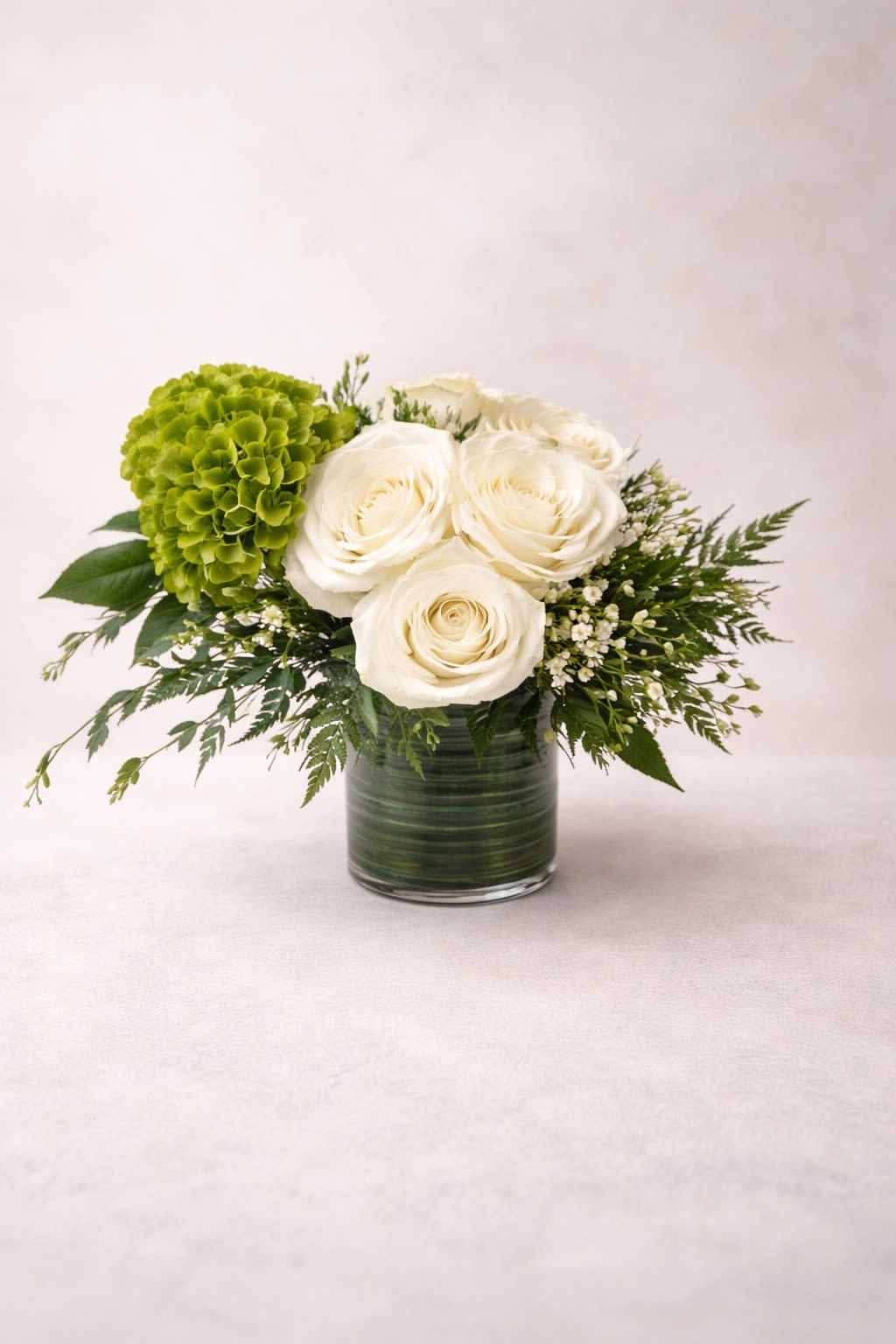 White roses and a green hydrangea in a glass vase