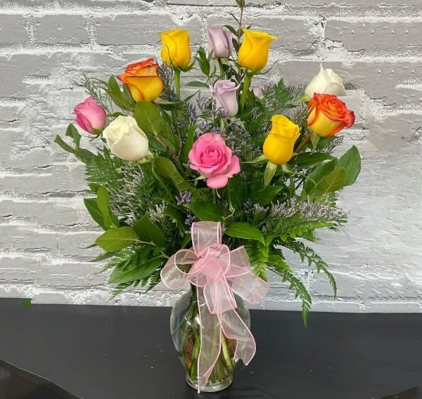 Bouquet of multicolored roses in a glass vase with a pink ribbon