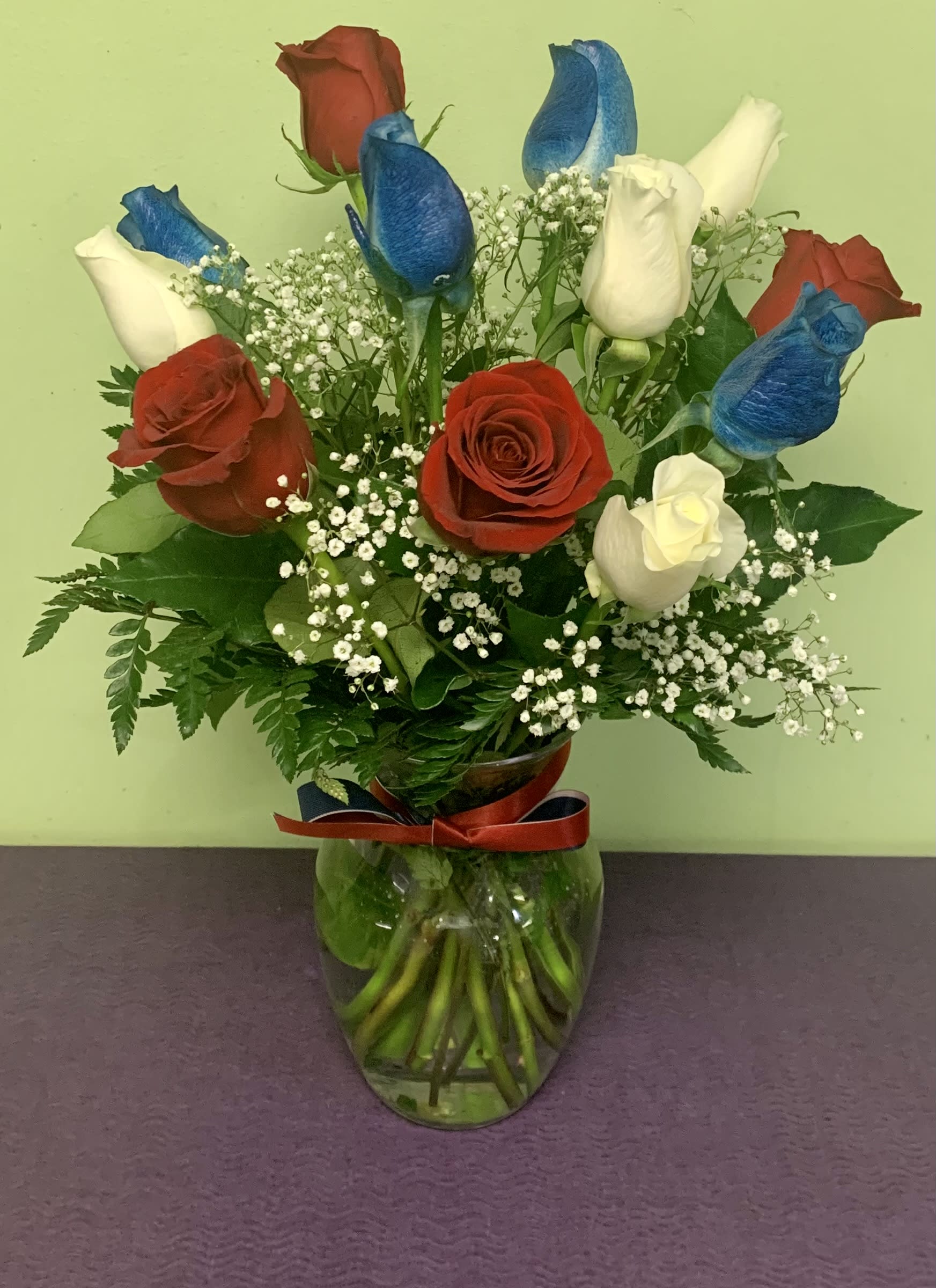 Red, white, and blue roses in a glass vase with baby's breath