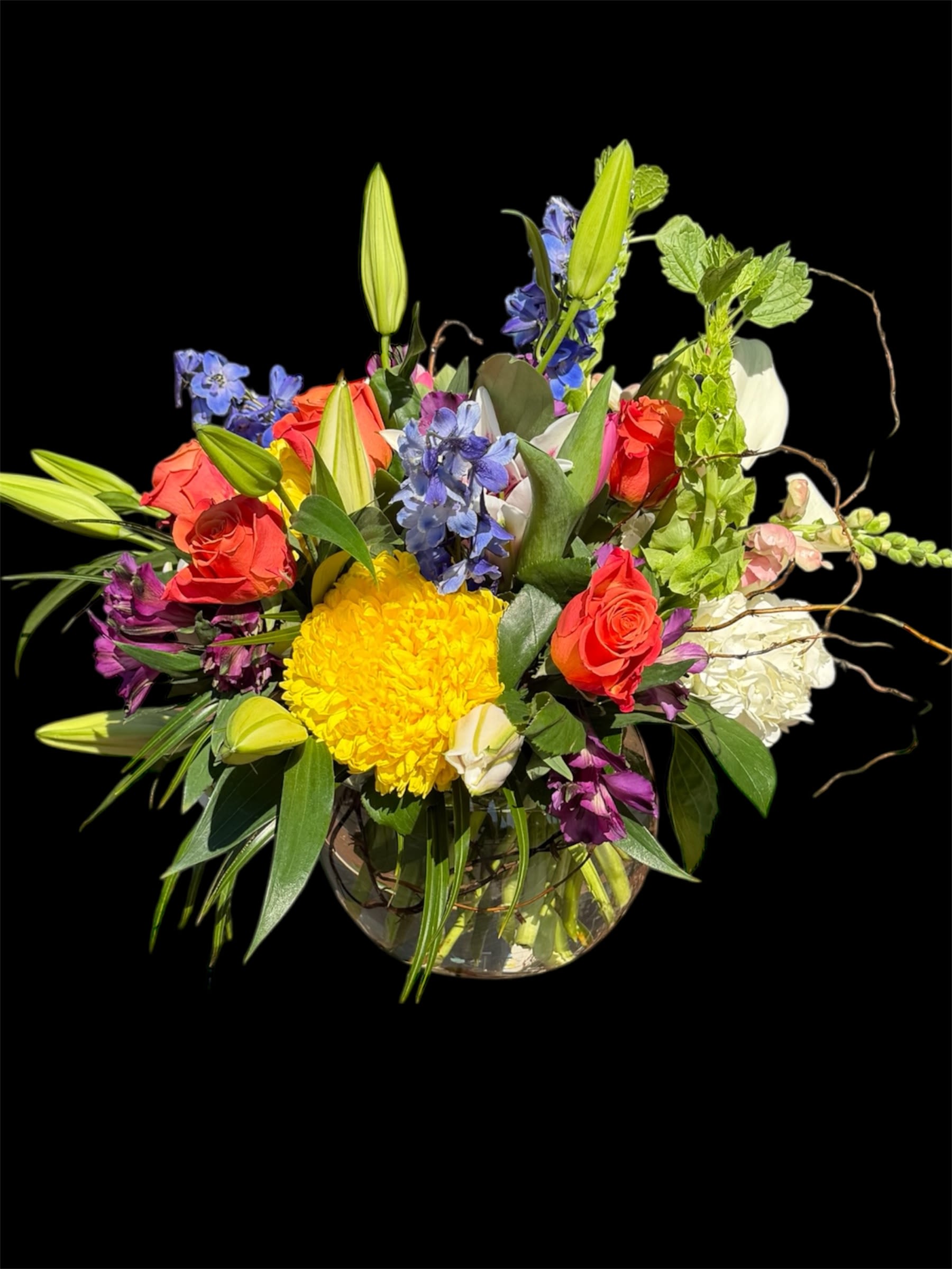 Rainbow Sensations - Rainbow sensation floral arrangement is a dynamic mix of bright, contrasting colors and various flower types, presented in a glass vase. The bouquet features a full spectrum of color, with blooms arranged in a garden-style design.  Includes: Vibrant Roses, Blue And Purple Accents, Yellow Focal Flowers, And Lilies And Greenery.