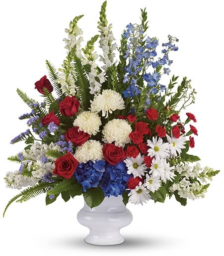 Large mixed flower arrangement in a white vase with red, white, and blue blooms