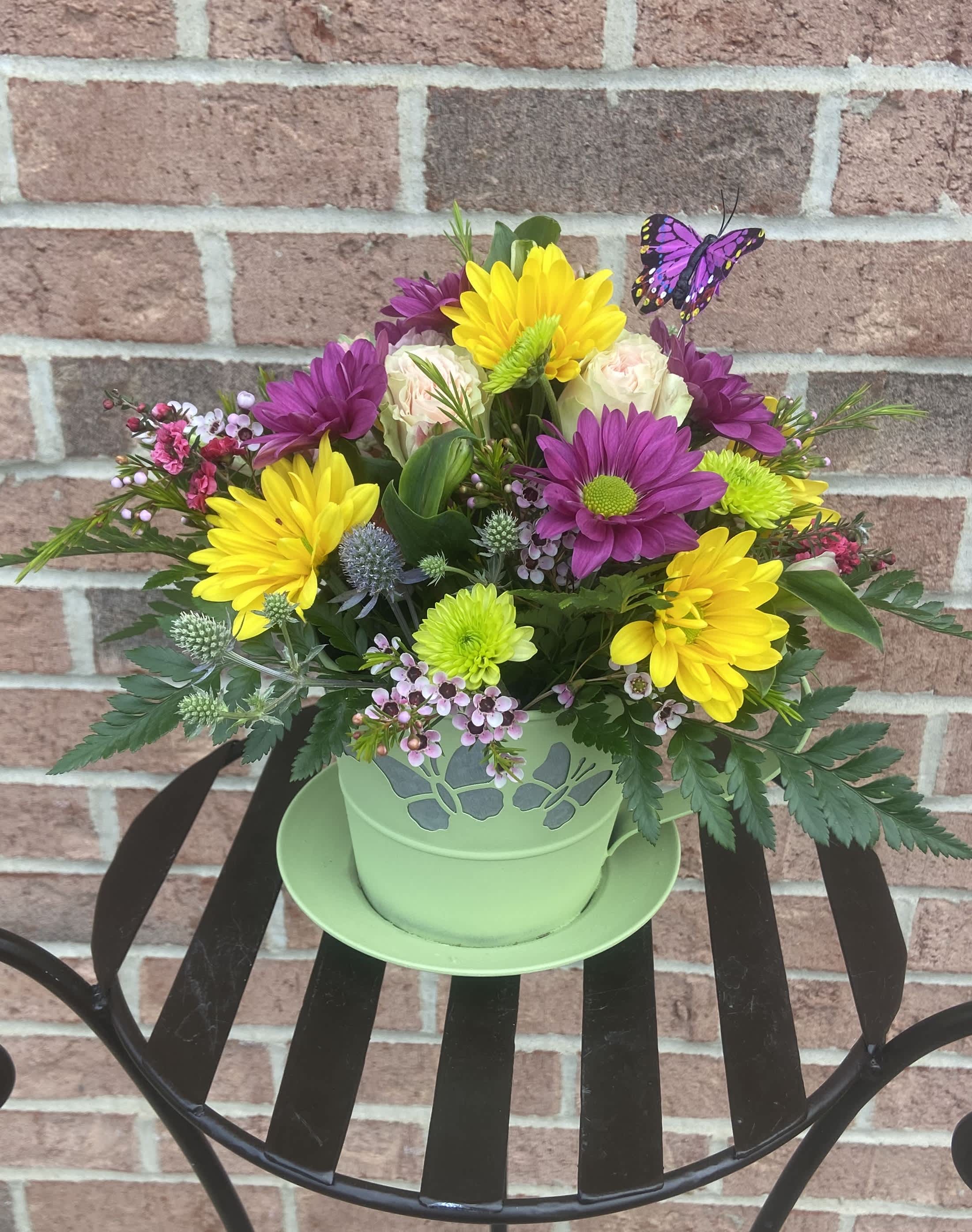 Colorful mixed flower arrangement in a green pot with a butterfly pick