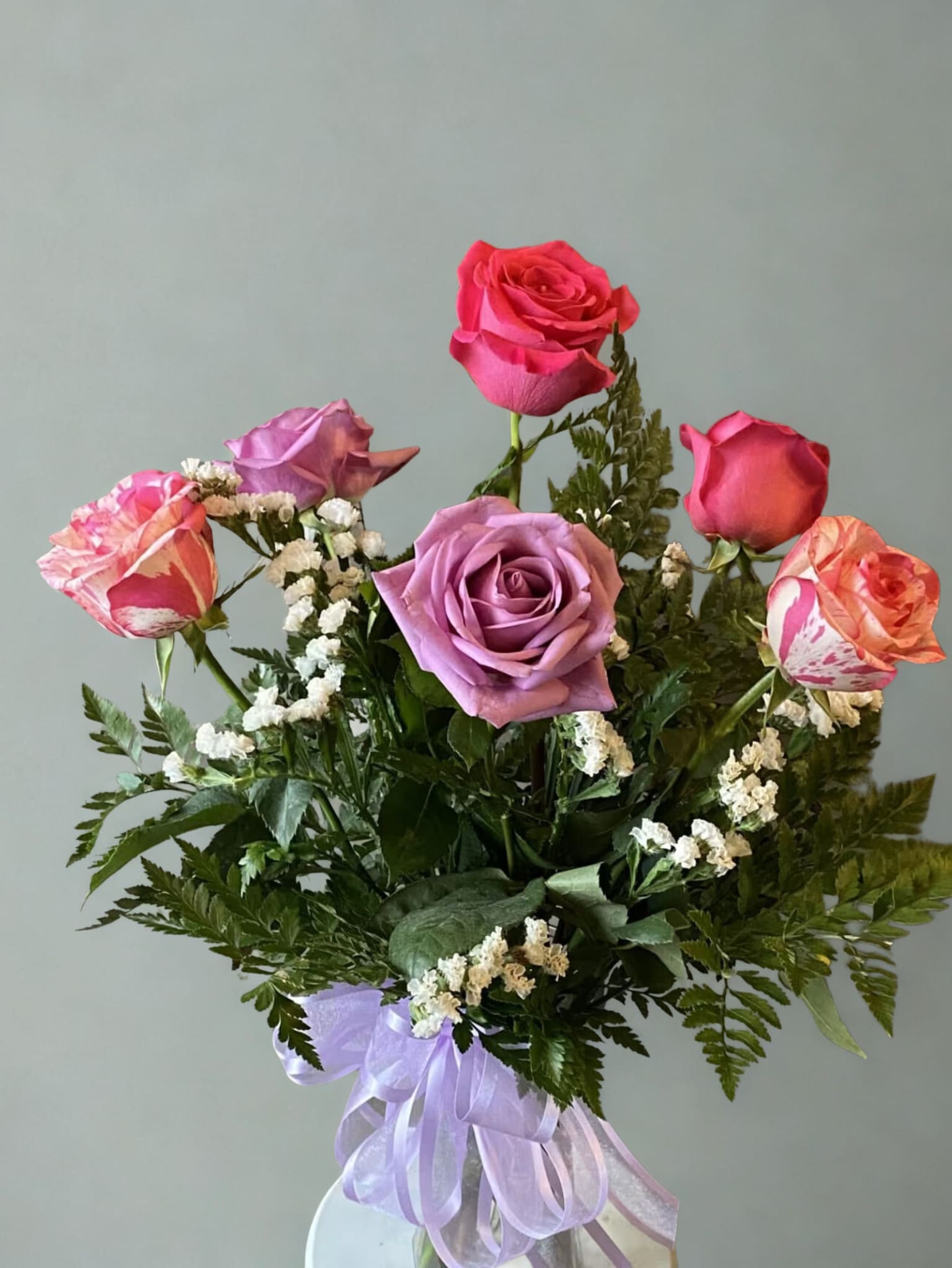 Bouquet of pink and lavender roses with white filler flowers and a purple ribbon
