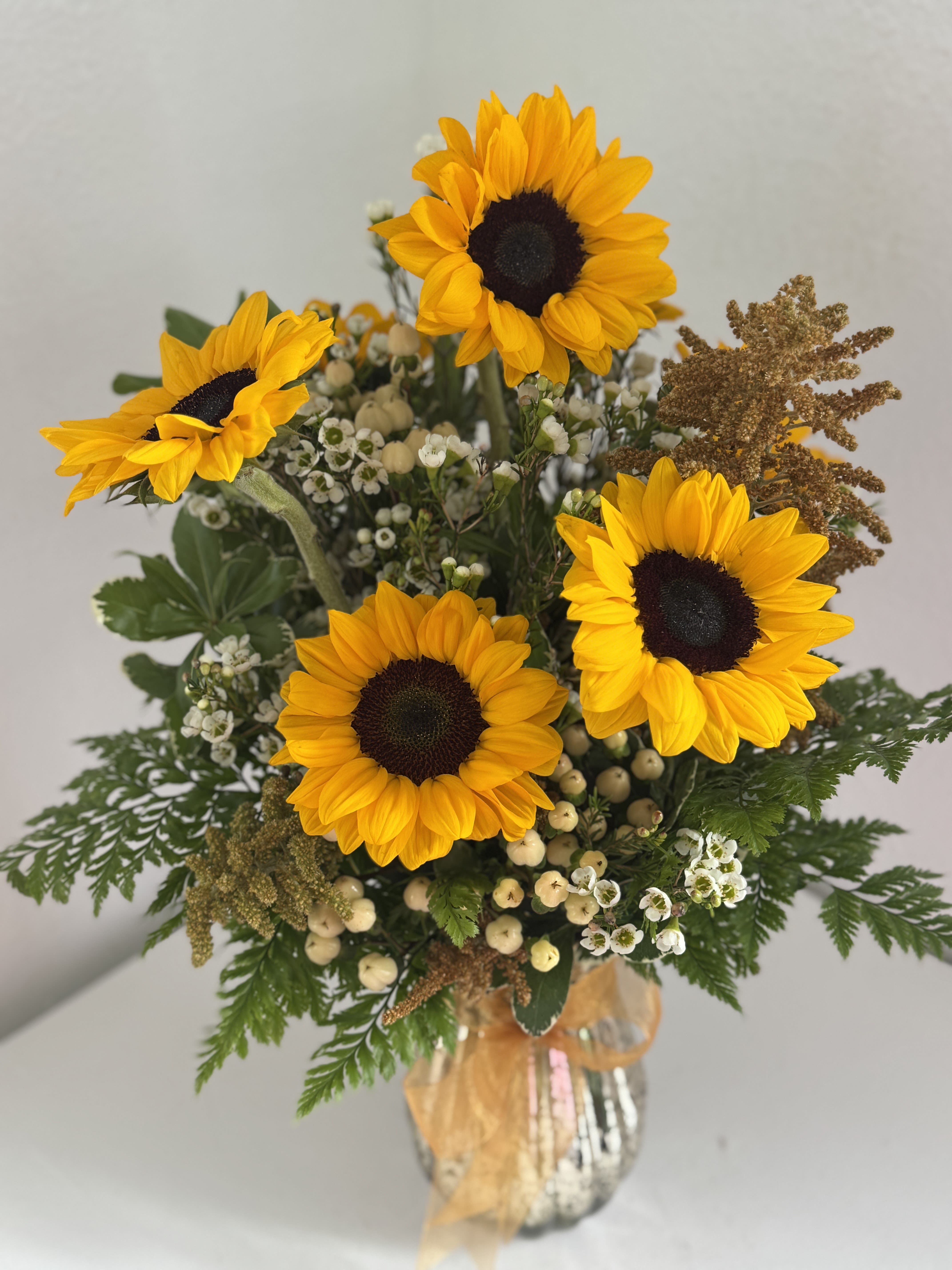 Sunflower Embrace **Container may vary** - Bright, bold, and full of joy, this arrangement captures the warmth of a heartfelt hug. Featuring radiant sunflowers surrounded by filler blooms and lush greenery, Sunflower Embrace brings sunshine and cheer into any space.