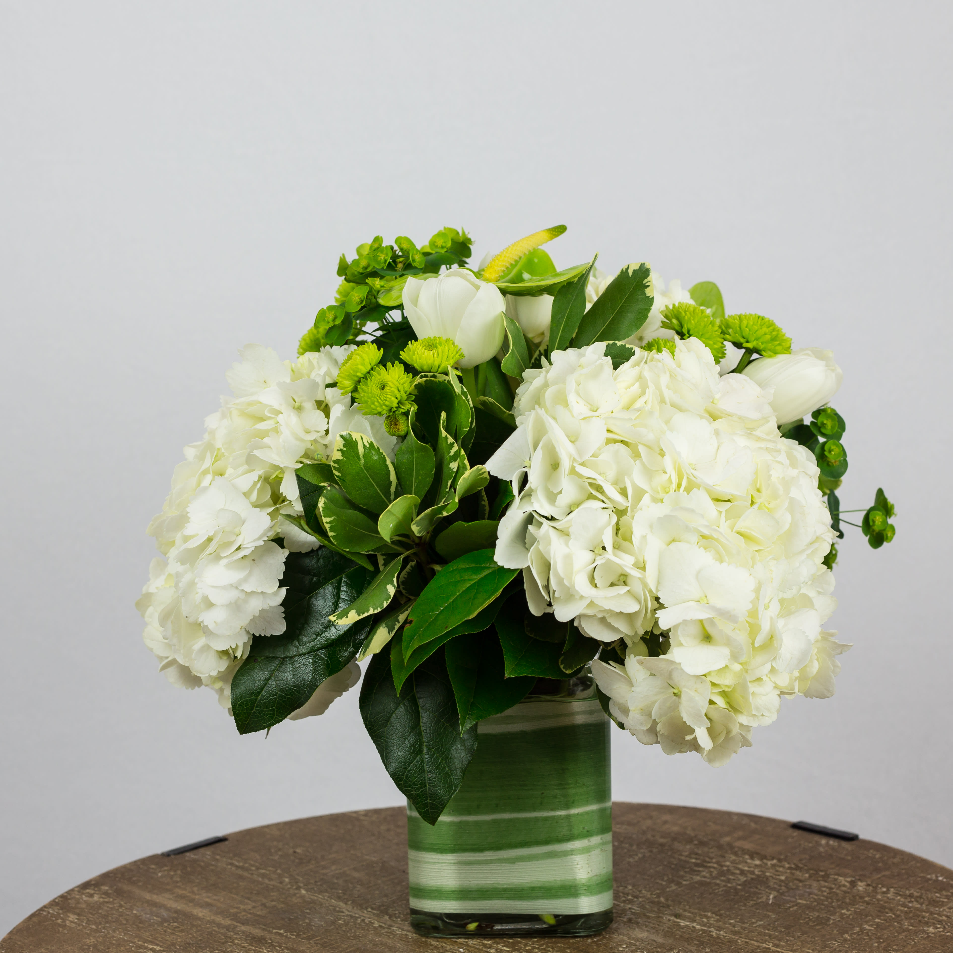 White hydrangeas and green flowers in a striped glass vase