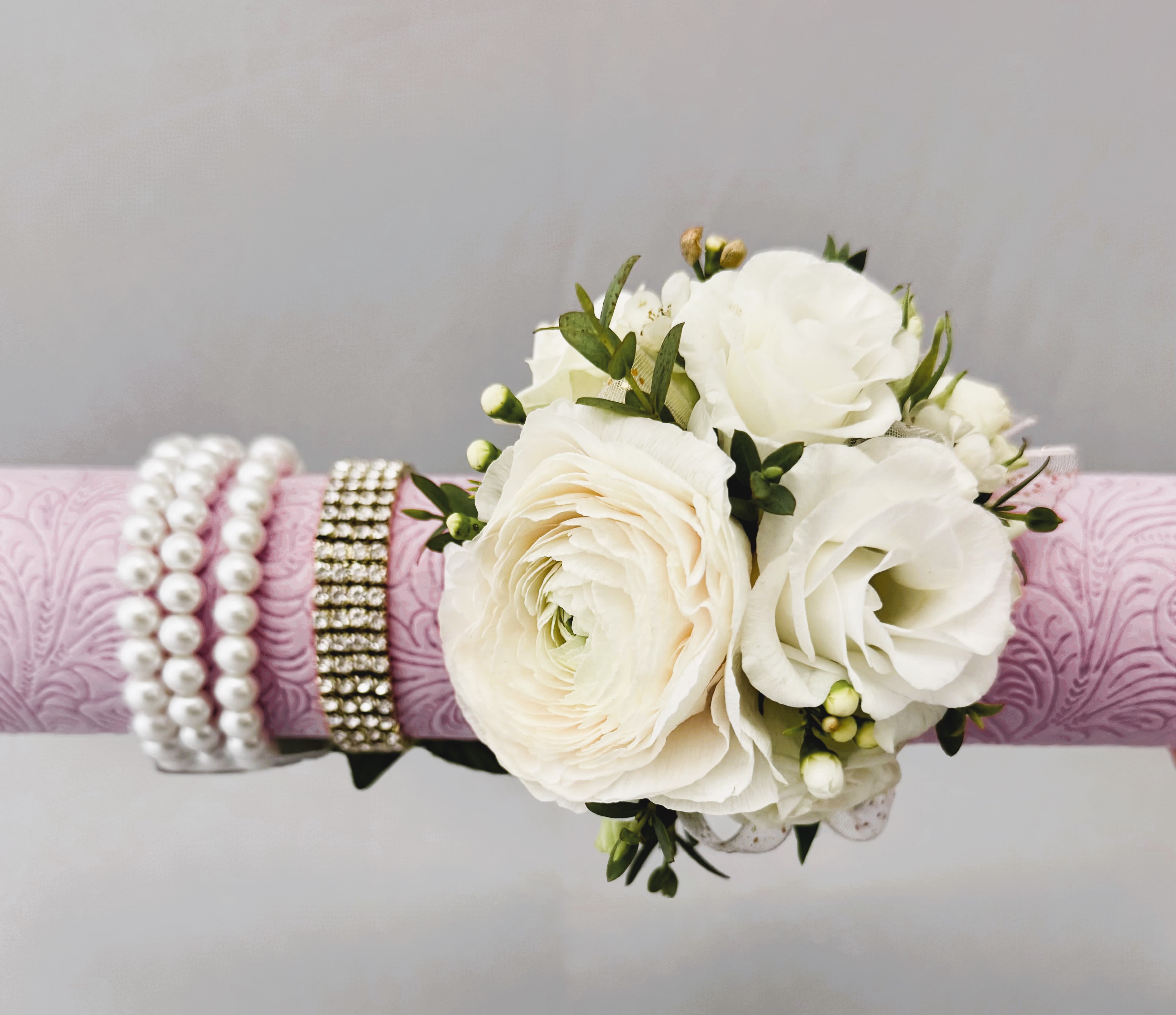 White floral wrist corsage on a pink patterned band with pearl and rhinestone bracelets
