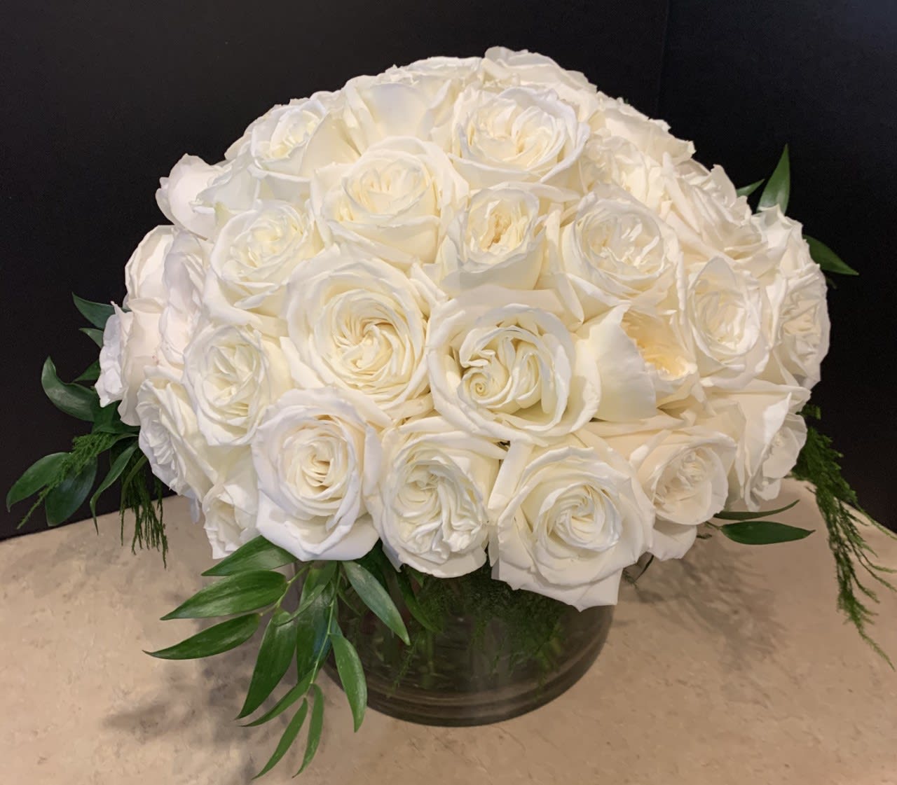 White rose bouquet in a low glass vase with green foliage