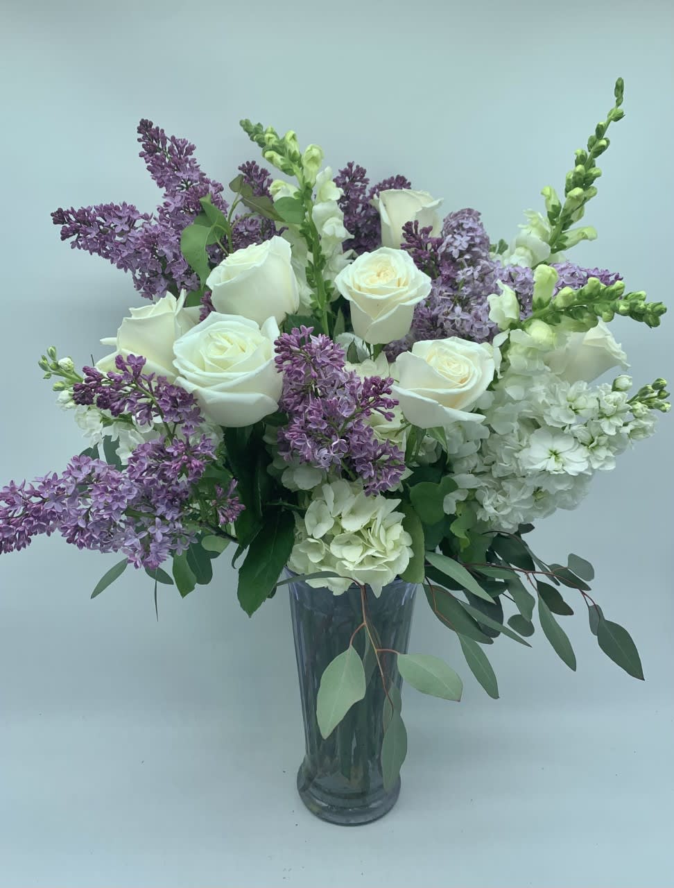 White roses and purple lilacs arranged in a clear glass vase