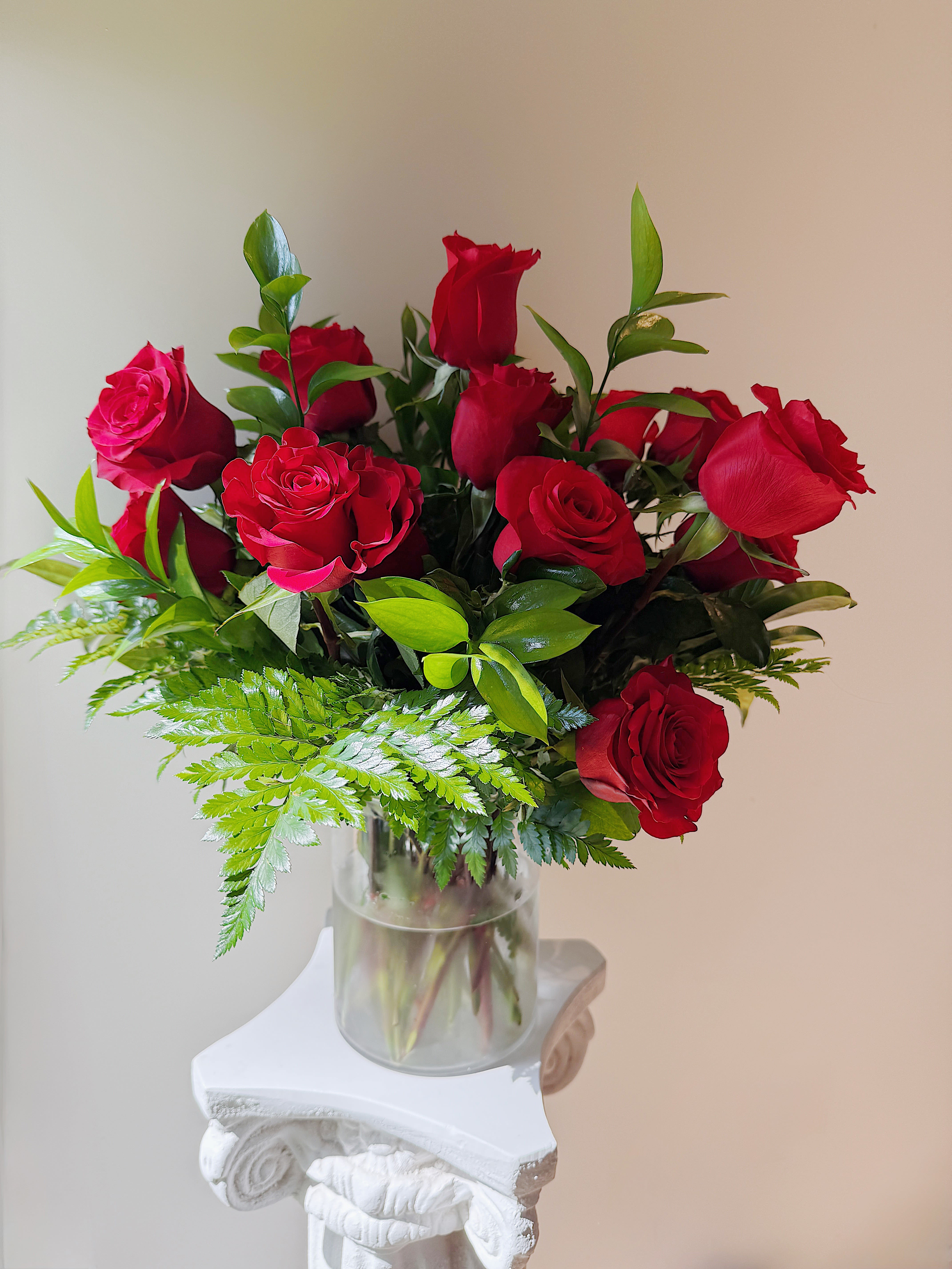 Red roses arranged in a clear glass vase with fern foliage
