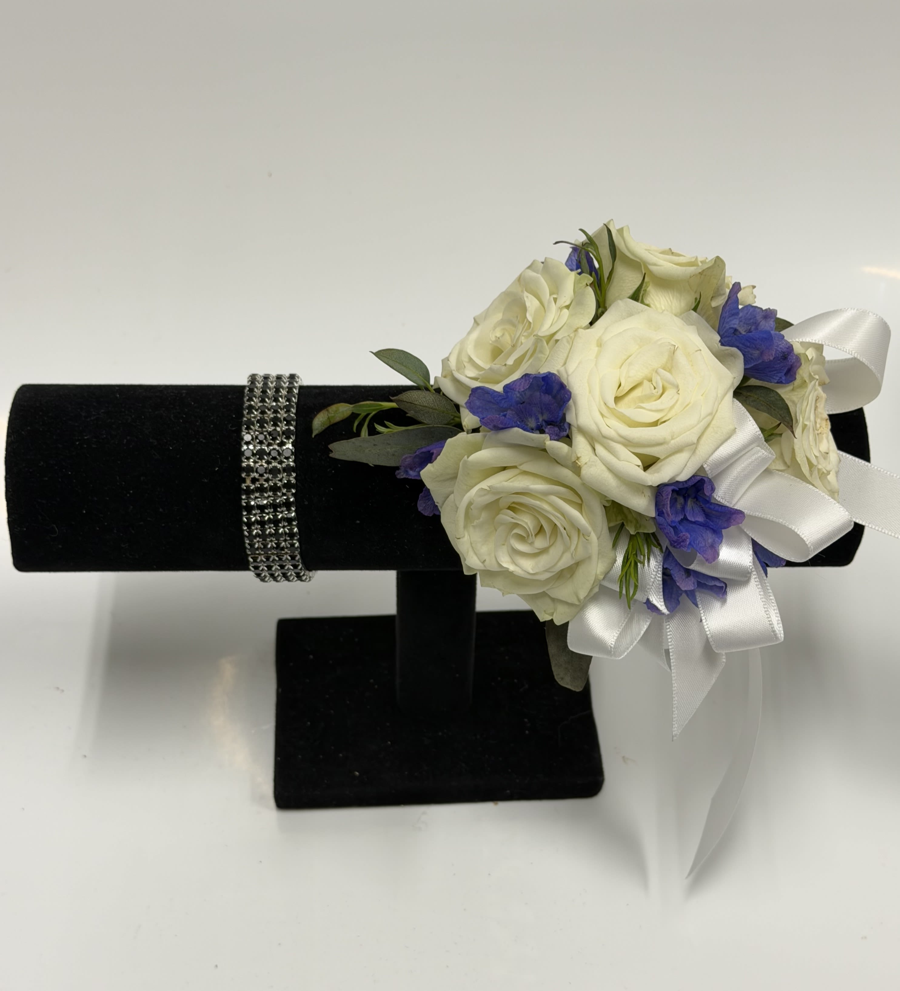 White Spray Rose and Blue Delphinium Corsage with Black Rhinestone Wristlet - White spray roses, sheer ribbon, blue delphinium, black rhinestone band, on a bed of greenery. Ribbon color can be customized, please specify in pick up note section. 