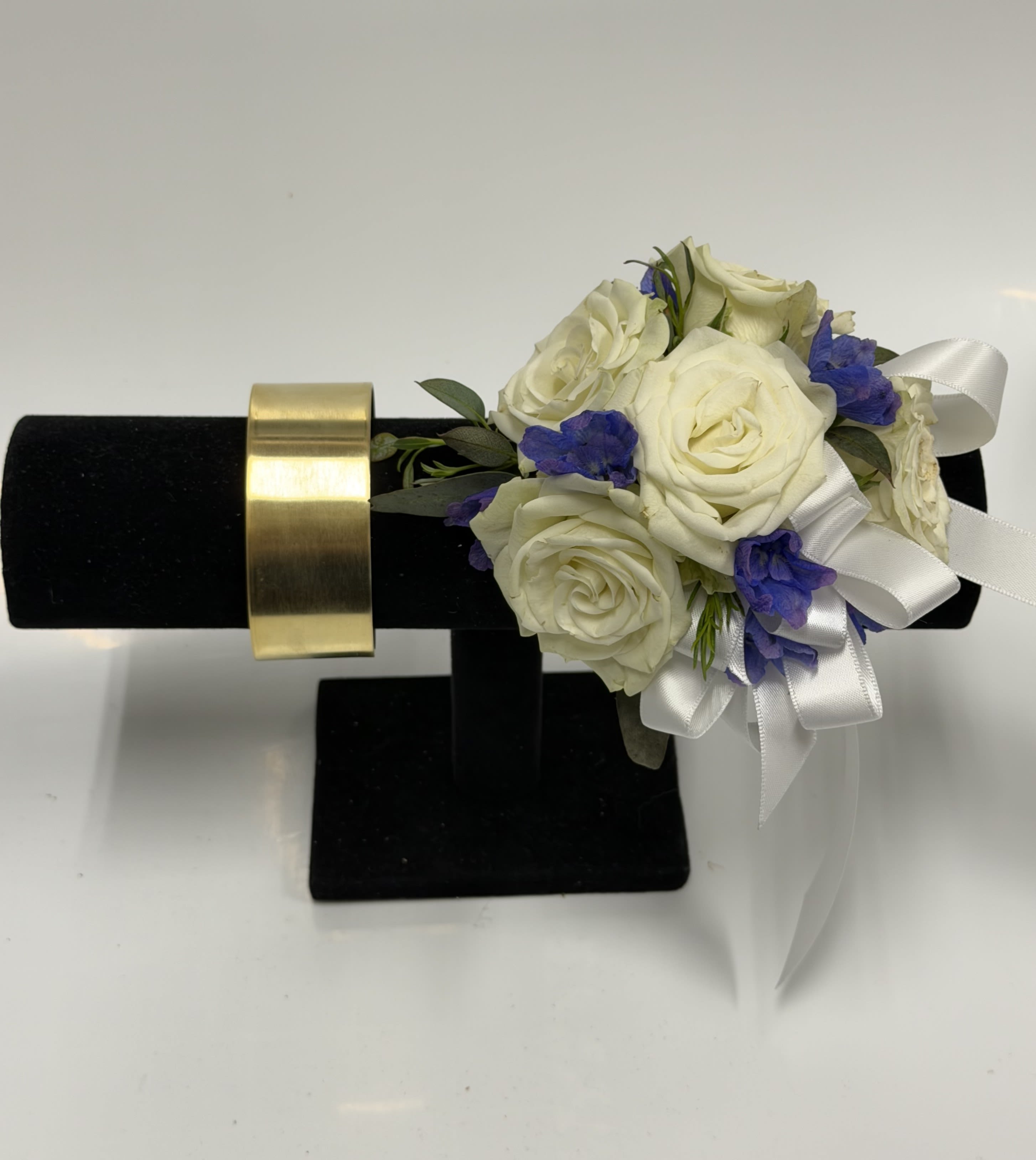 White Spray Rose and Blue Delphinium Corsage with Gold Cuff Wristlet  - White spray roses, sheer ribbon, blue delphinium, gold cuff wristlet,  on a bed of greenery.  Ribbon color can be customized; please specify in the pick-up note section. 