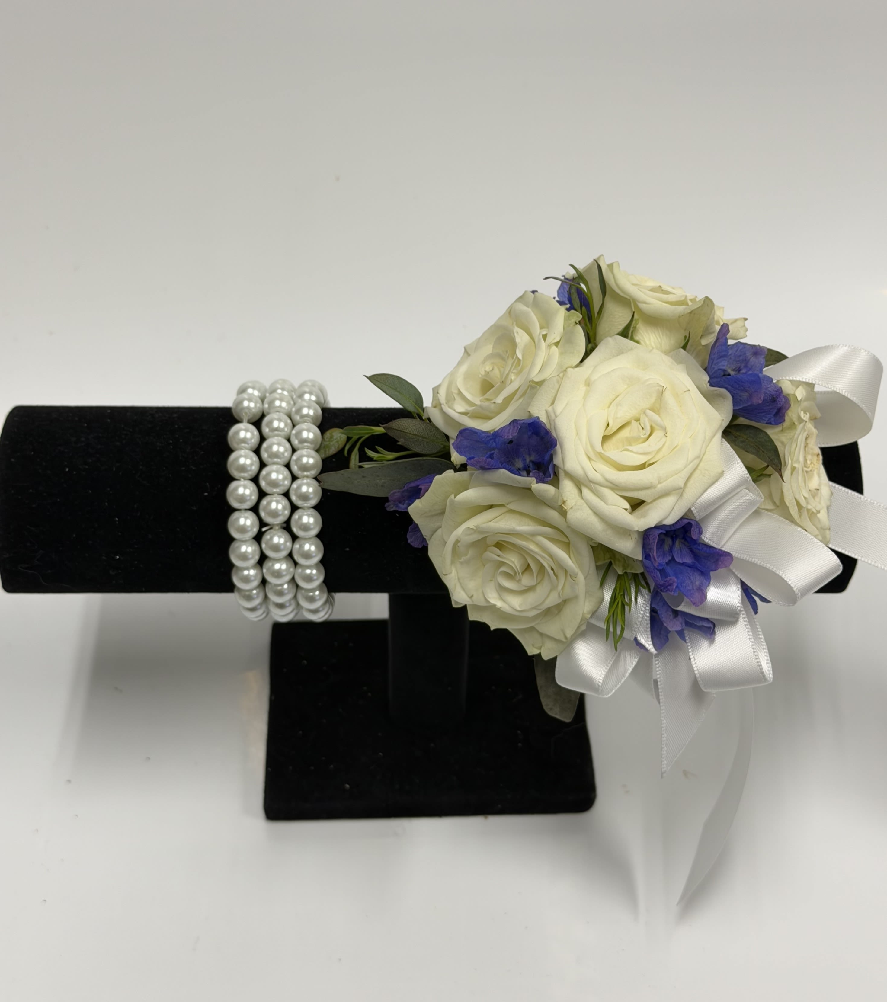 White Spray Rose and Blue Delphinium Corsage with Pearl Wristlet - White spray roses, sheer ribbon, blue delphinium on a bed of greenery. Ribbon color can be customized, please specify in pick up note section. 