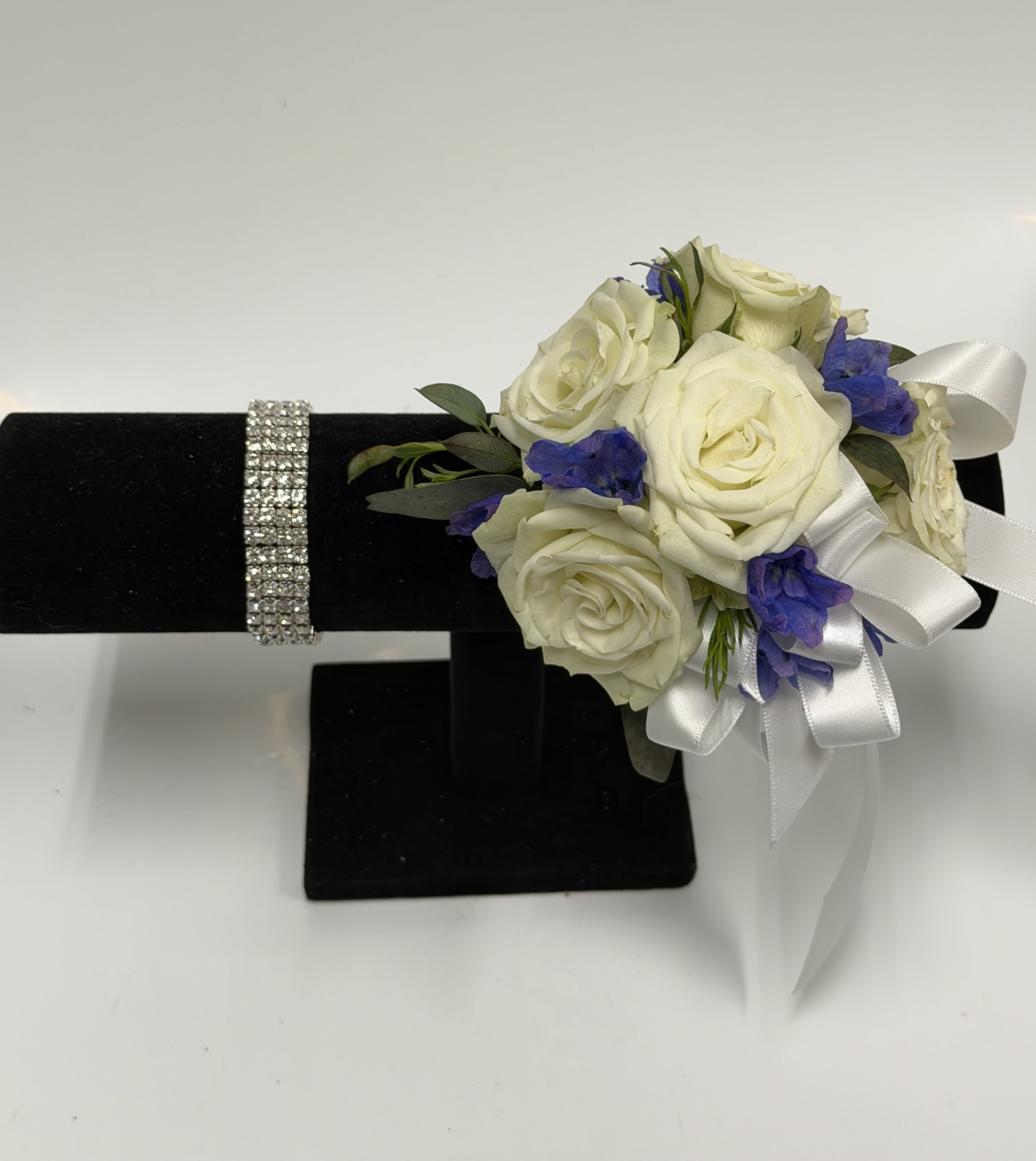 White Spray Rose and Blue Delphinium Corsage with Silver Rhinestone Wristlet - White spray roses, sheer ribbon, silver rhinestone band,  blue delphinium on a bed of greenery. Ribbon color can be customized, please specify in the pick-up note section. 